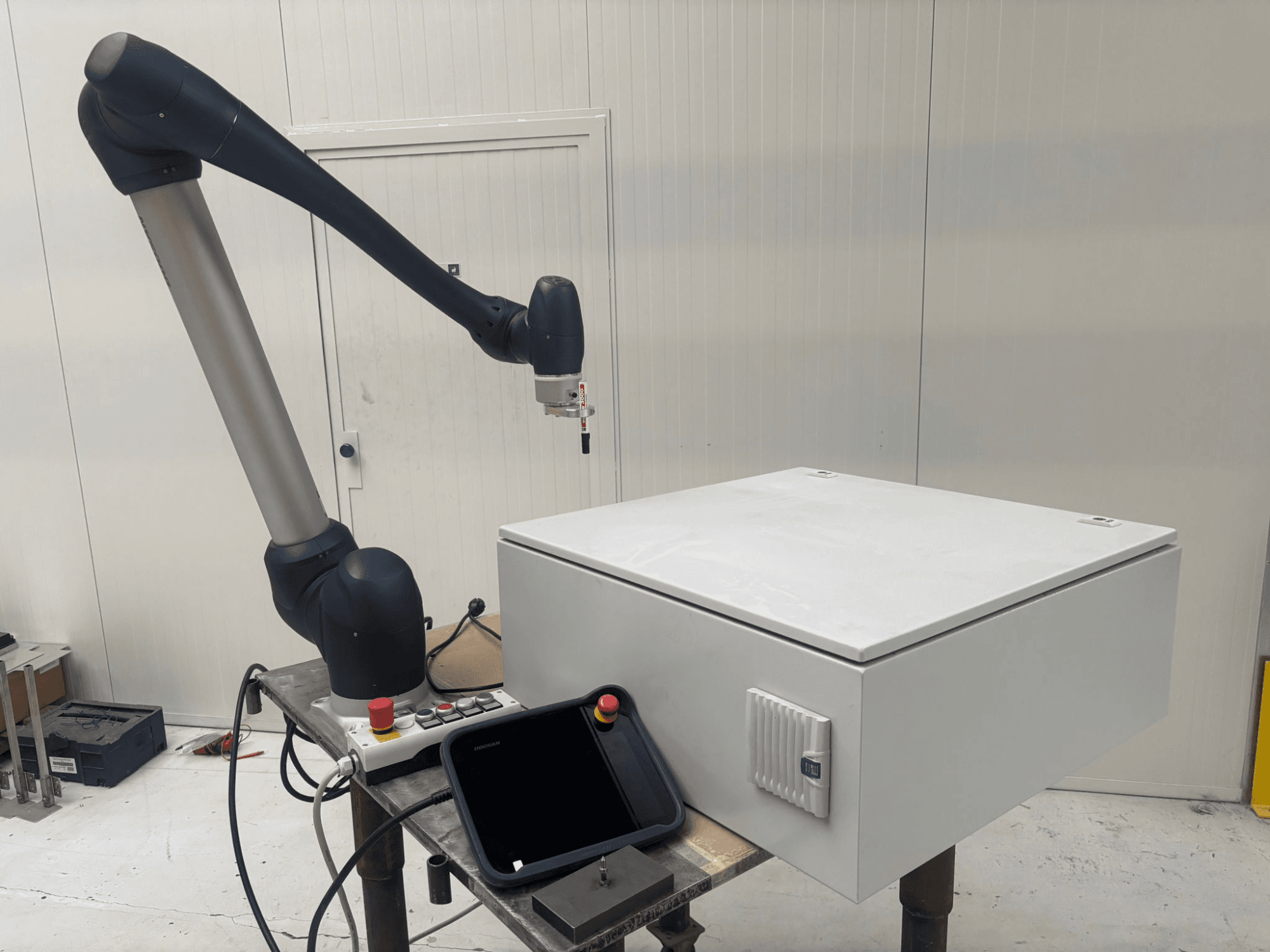 Kollaborationsroboter DOOSAN M0617 in Seitenansicht, mit ausgefahrenem Roboterarm über einer Steuerungsschnittstelle und einer weißen Box auf einem Tisch.