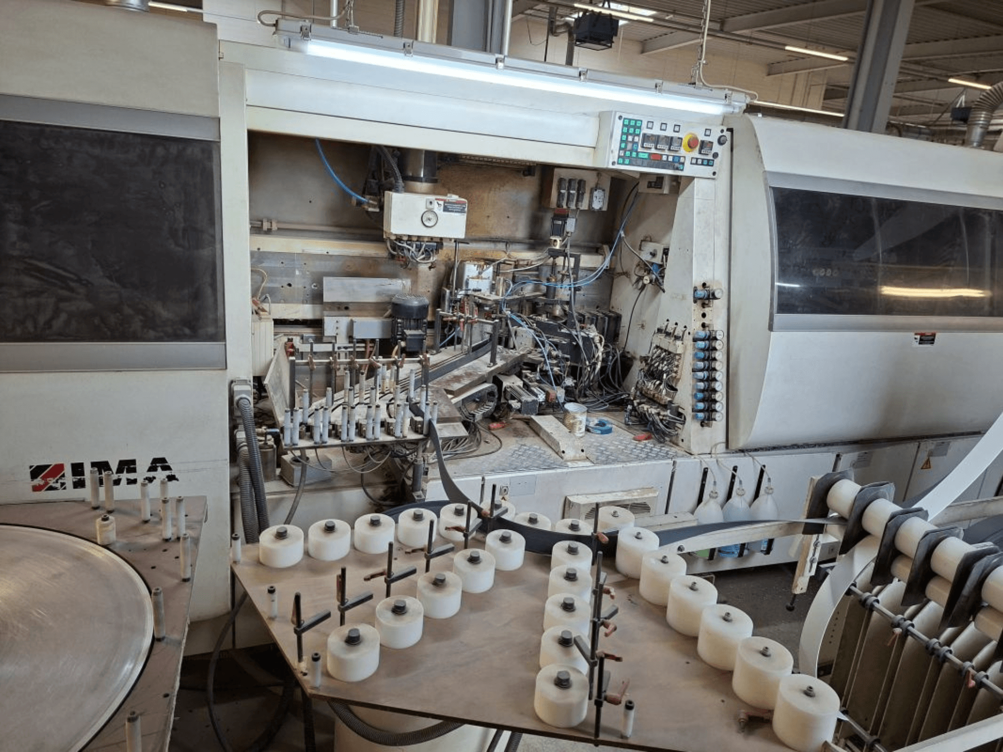 IMA machinery viewed from the side, showcasing complex mechanical components and a round table with white spools.
