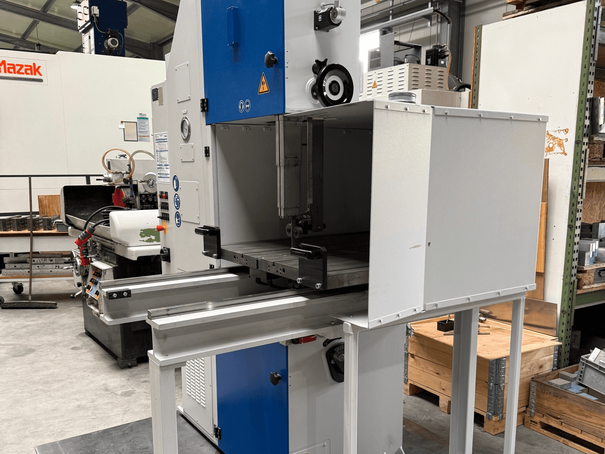 Mazak-Industriemaschine von vorne gesehen mit blauem Bedienfeld, Metalltisch und Sicherheitshinweisen.