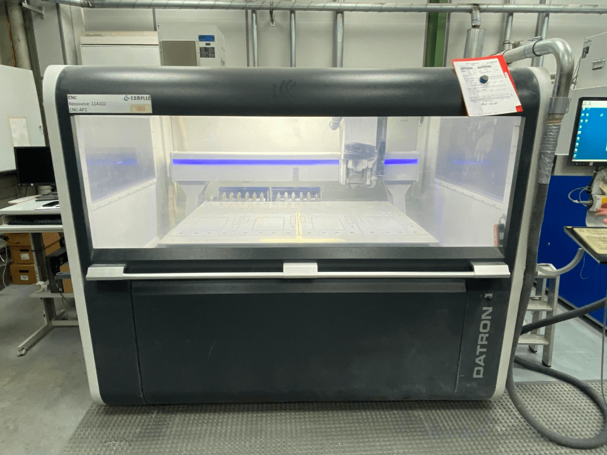 Frontansicht eines Datron MLCube B Vertikal-Bearbeitungszentrums mit sichtbaren Bedienelementen und einem Arbeitstisch in einer Werkstattumgebung.