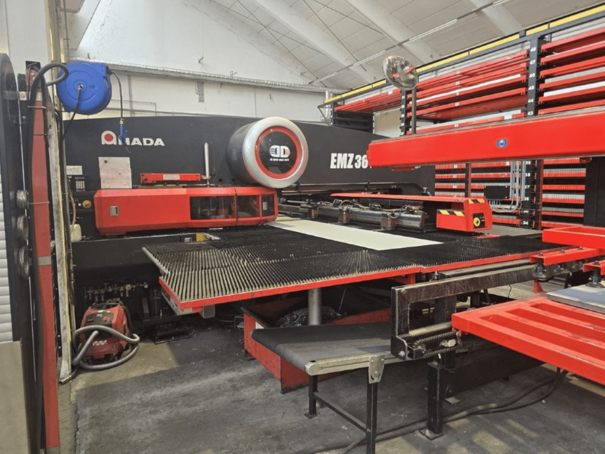 Amada EMZ 36 laser cutting machine in a workshop, front view, featuring red accents and a large cutting table.