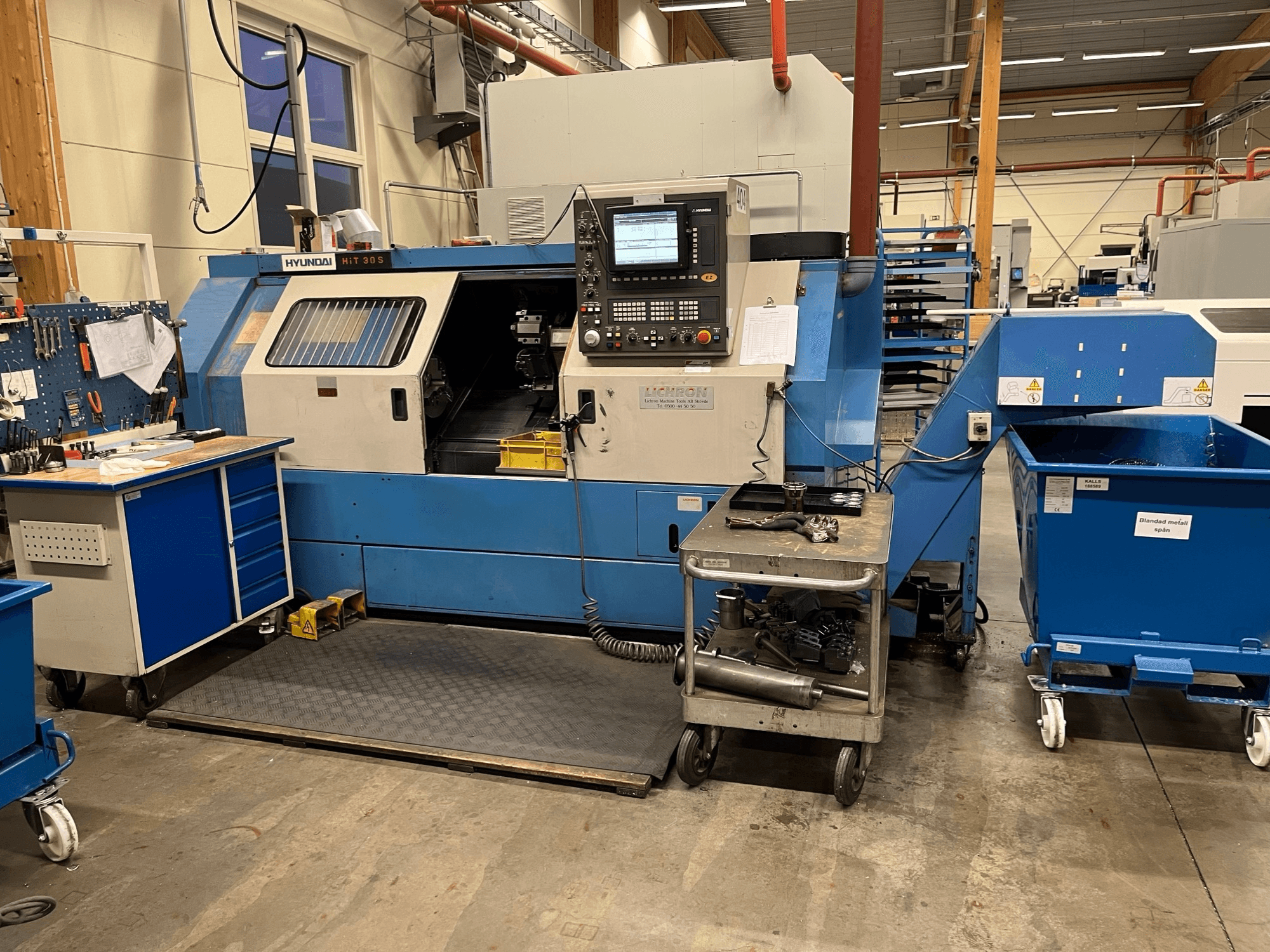 Hyundai HIT 30S Horizontaldrehmaschine, Vorderansicht, mit Bedienfeld und Werkzeugen auf einem nahegelegenen Wagen in einer Werkstattumgebung.