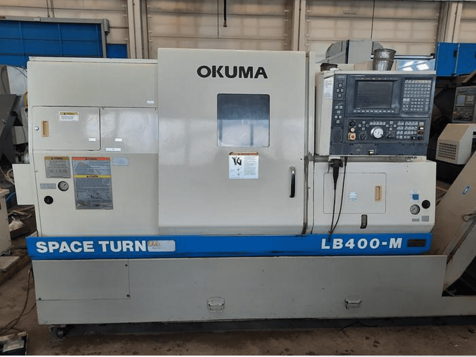 Okuma LB400-M CNC-Drehmaschine, Vorderansicht mit Bedienfeld, Warnschildern und blauem "SPACE TURN"-Schriftzug sichtbar.