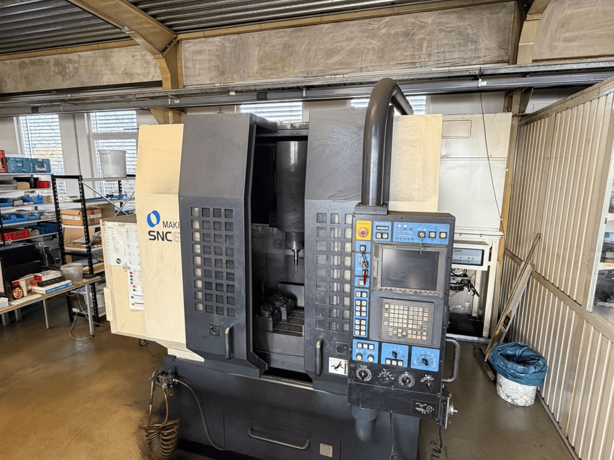 Vertikales Bearbeitungszentrum Makino SNC 64-A15 in der Vorderansicht mit Bedienfeld, Bearbeitungsbereich und Industriearbeitsplatz.