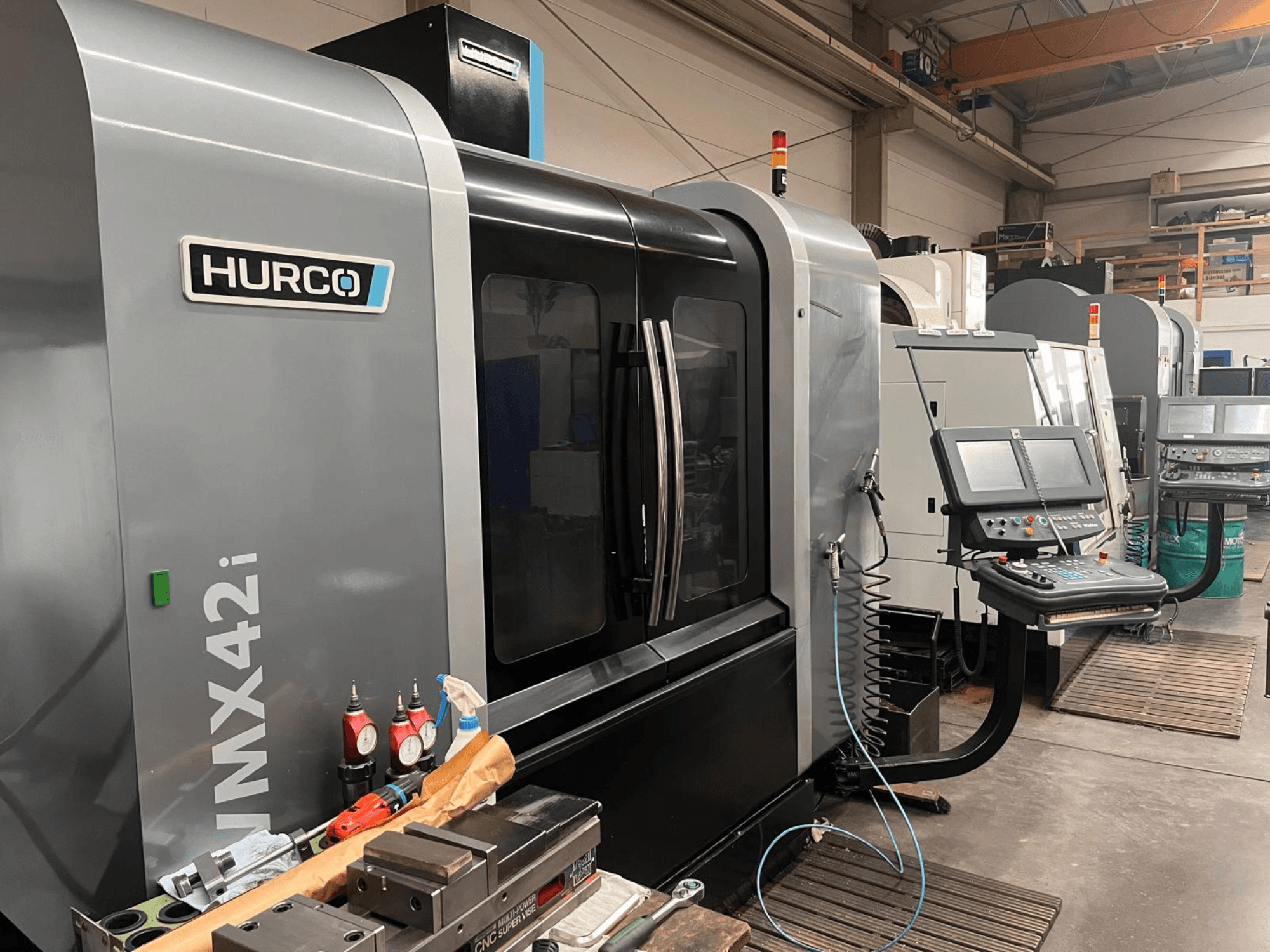 Hurco VMX42i CNC-Maschine in einer Werkstatt, Vorderansicht, mit Bedienfeld und verschiedenen Werkzeugen auf der Werkbank.