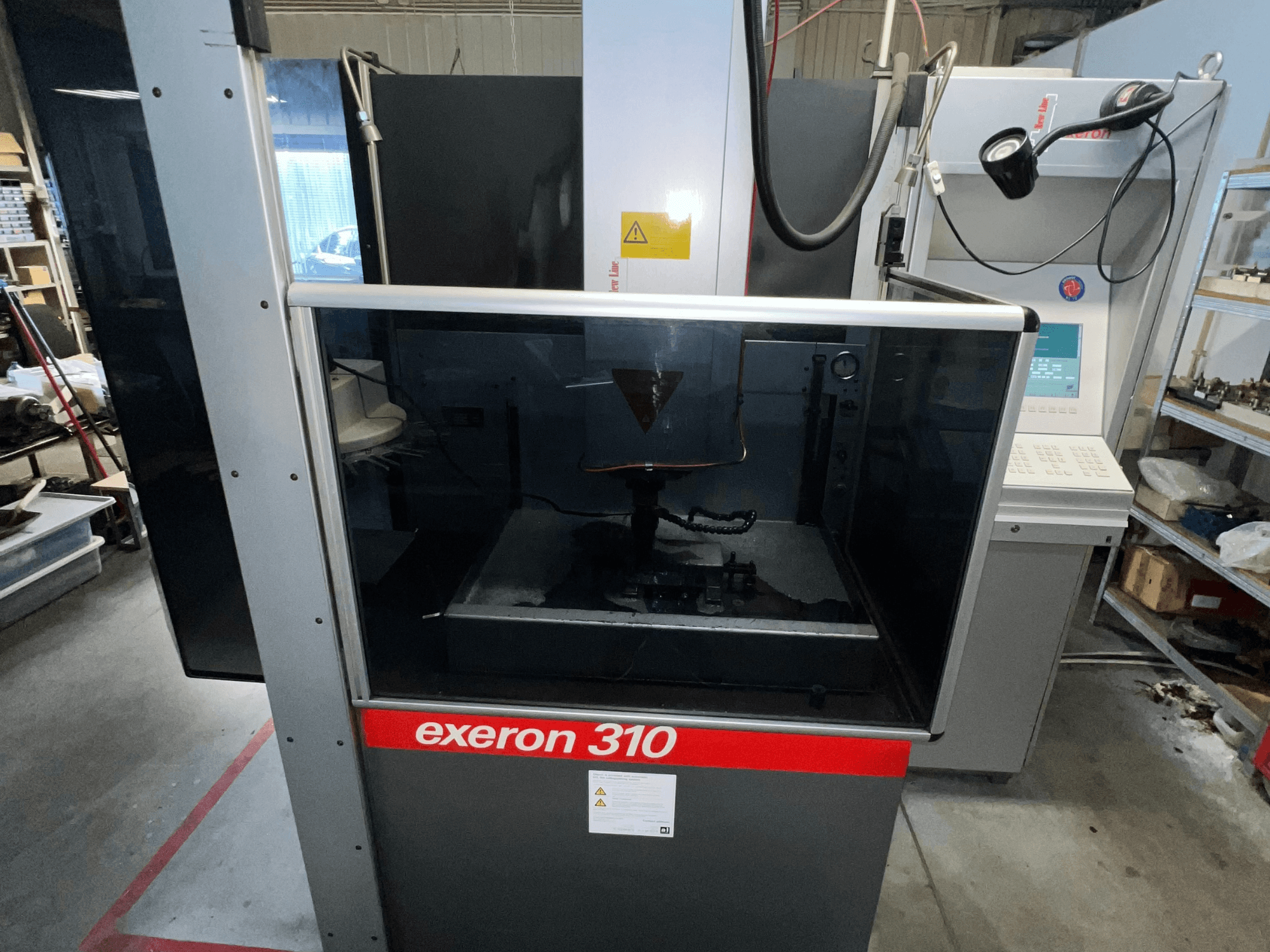 Vorderansicht einer Exeron 310 Maschine mit Glaskammer und Bedienfeld sowie Regalen am Arbeitsplatz.