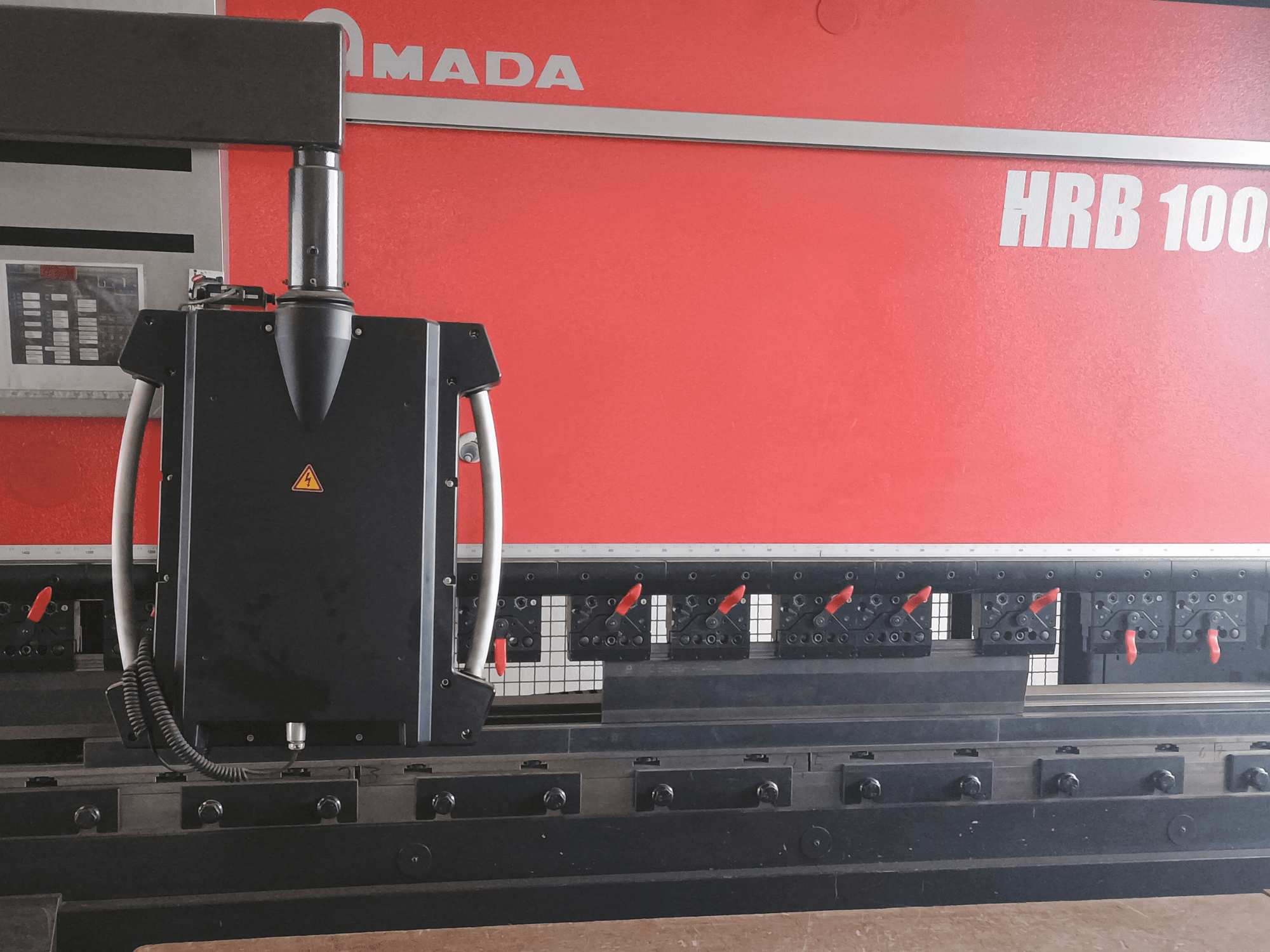 Amada HRB 100 Biegemaschine in der Vorderansicht; mit schwarzem Steuerkopf mit konischer Düse und verstellbaren Spannern.