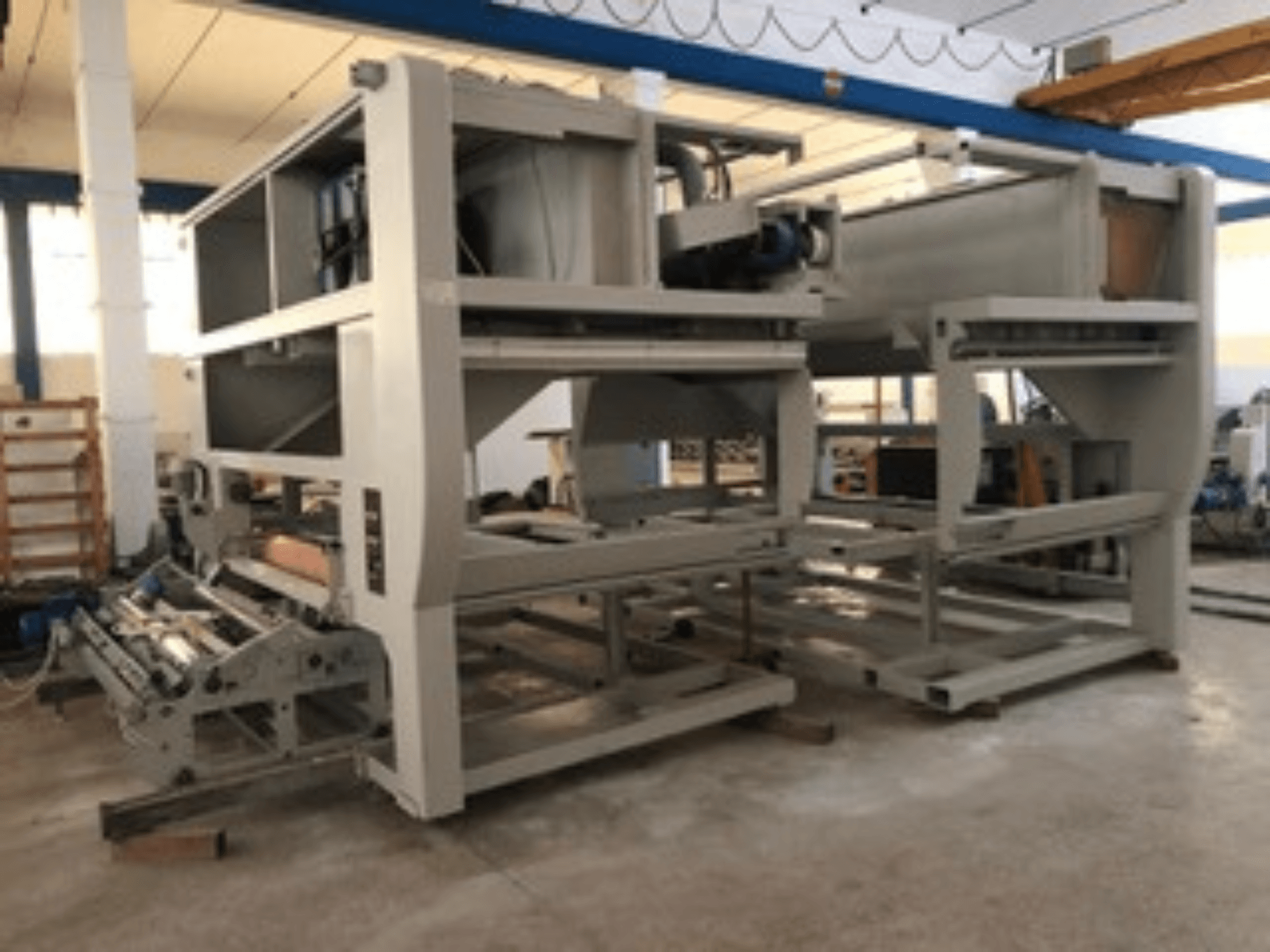 Industrial machine with multiple conveyor rollers and large structure; side view, gray color, located in a well-lit factory.