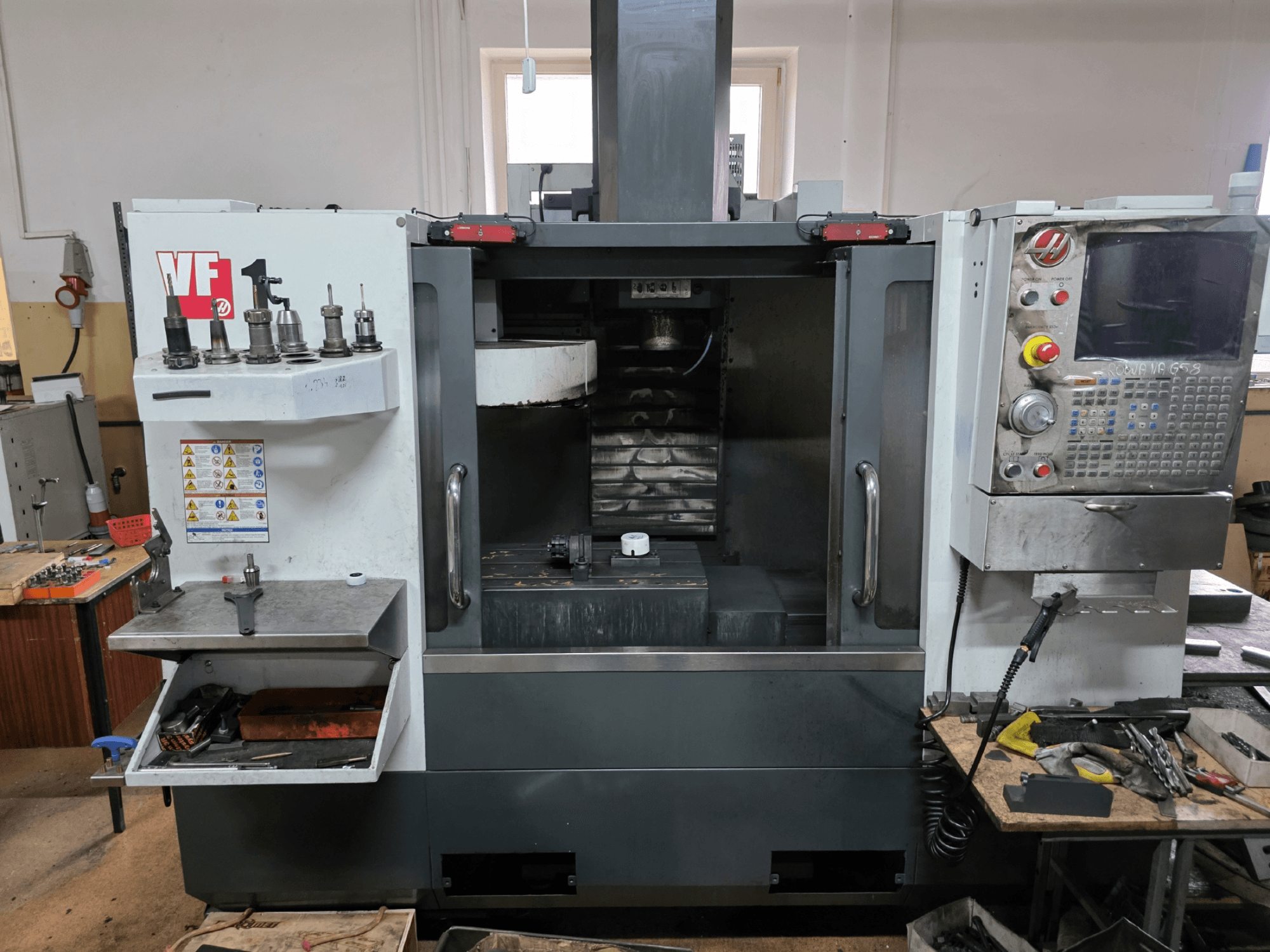 Haas VF series CNC milling machine, front view; features multiple tool holders, control panel, and visible work area.