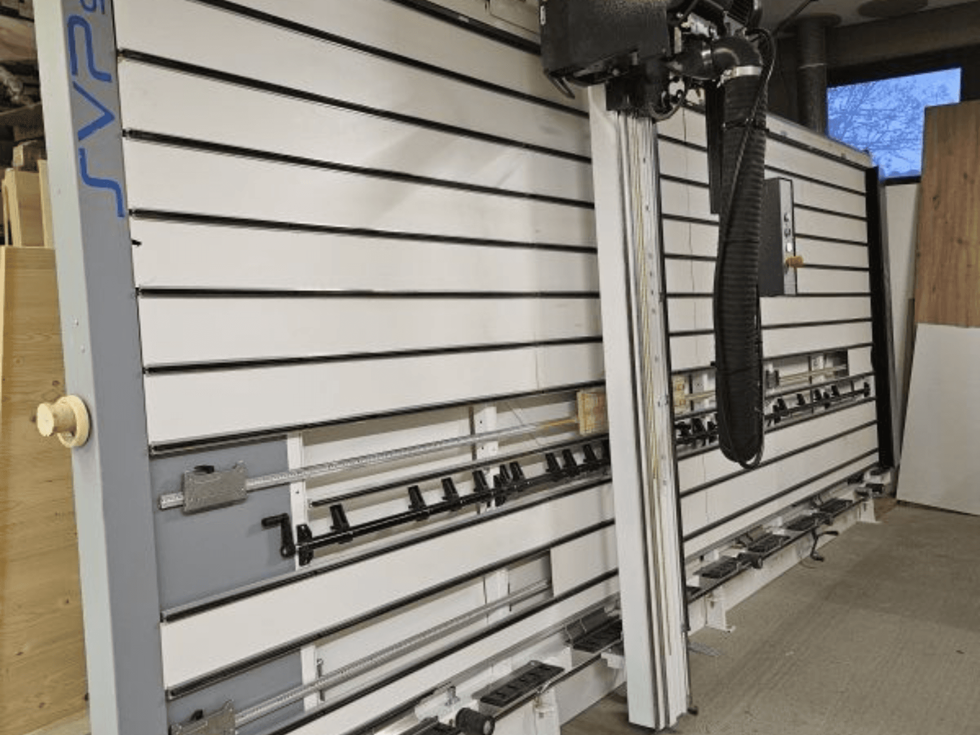 SVP-Schiebeplattensäge in einer Werkstatt, Vorderansicht, mit verstellbaren Führungsschienen und einer Staubabsaugung über Kopf.