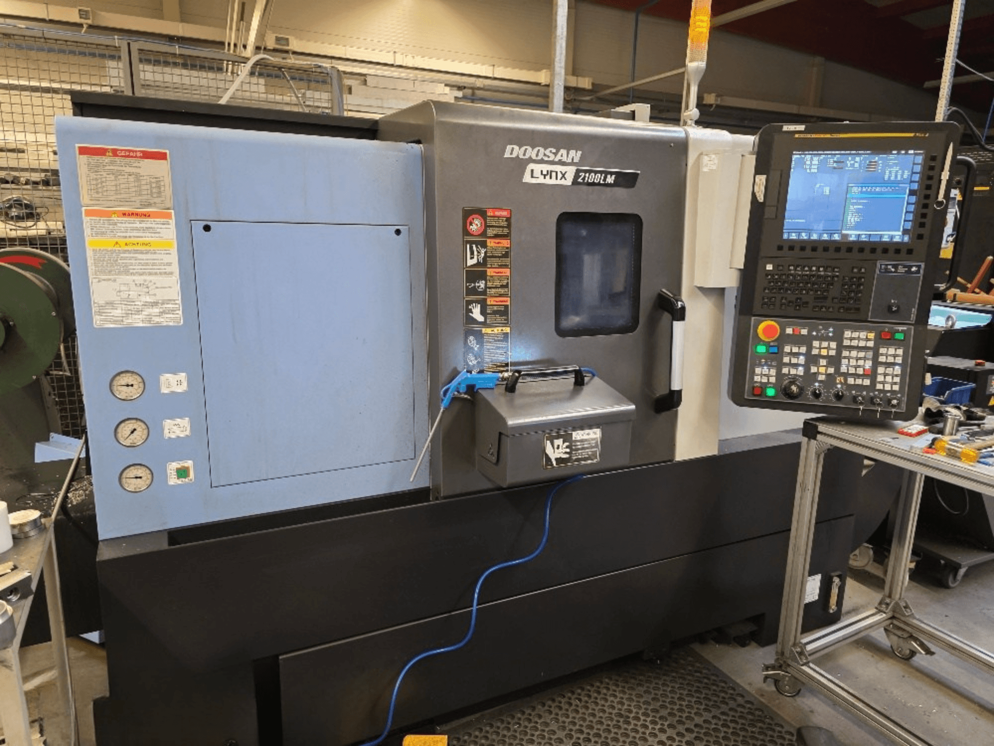 Doosan Lynx 2100LM CNC lathe, front view, featuring a control panel, pressure gauges, and safety warnings.