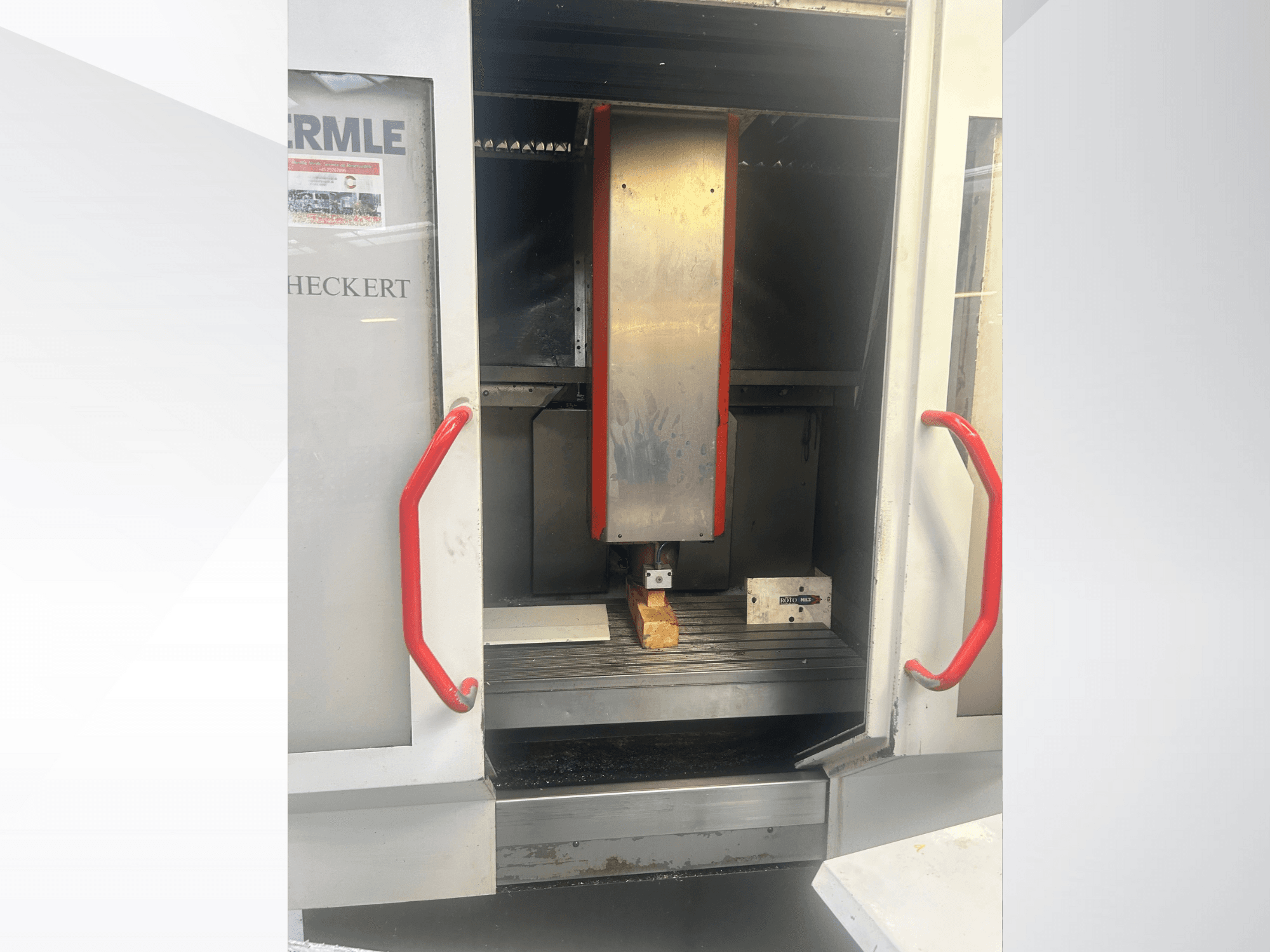 Frontansicht der Hermle CNC-Maschine mit metallischem Innenraum, roten Griffen und einem Werkstück auf dem Tisch.