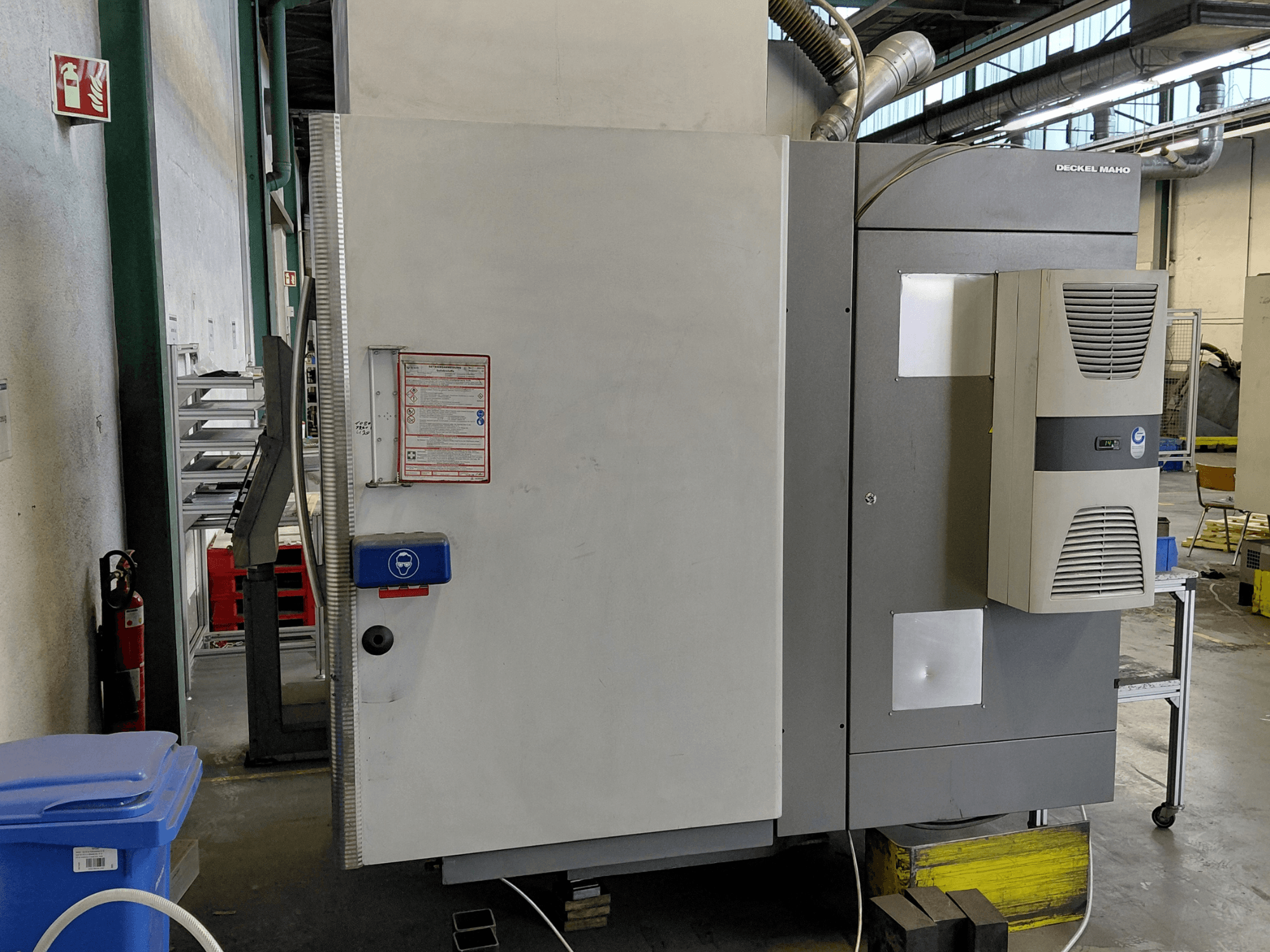 Seitenansicht des vertikalen Bearbeitungszentrums DECKEL MAHO DMC 635 V mit sichtbarem Bedienfeld und Sicherheitsschildern.