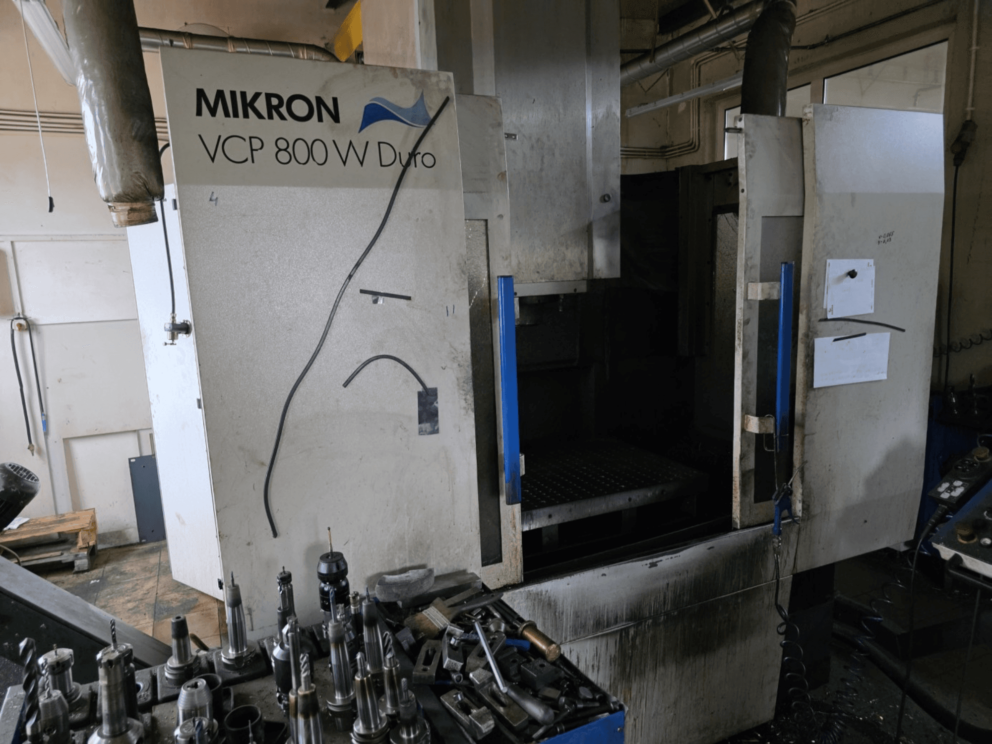 Mikron VCP 800 W Duro milling machine shown from a side view, with tools and controls visible in the foreground.