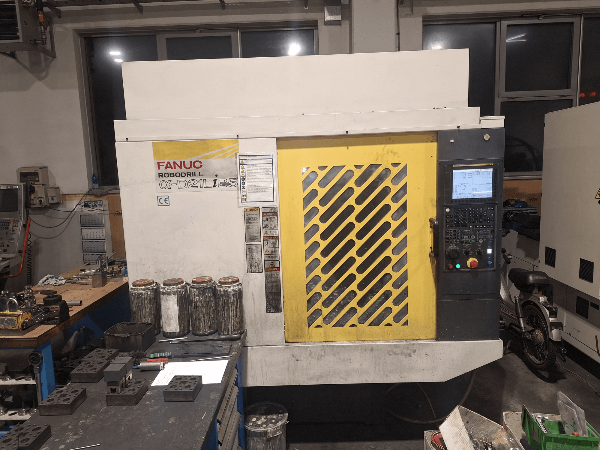 Vorderansicht des FANUC Robodrill α-D21LiB5, mit Bedienfeld, gelbem Gitter und Werkzeugen in der Nähe auf einer Werkbank.