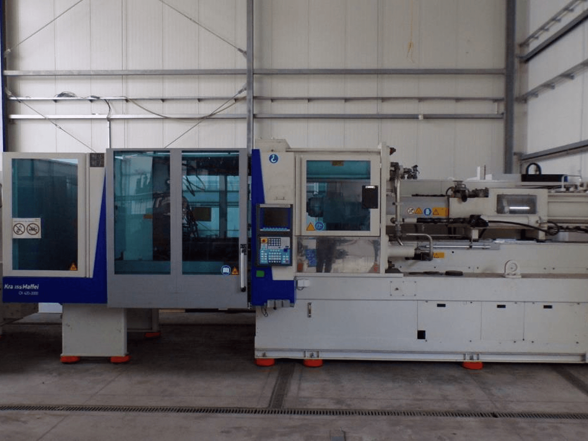 KraussMaffei injection molding machine, side view, features control panel and safety indicators, visible in a factory setting.