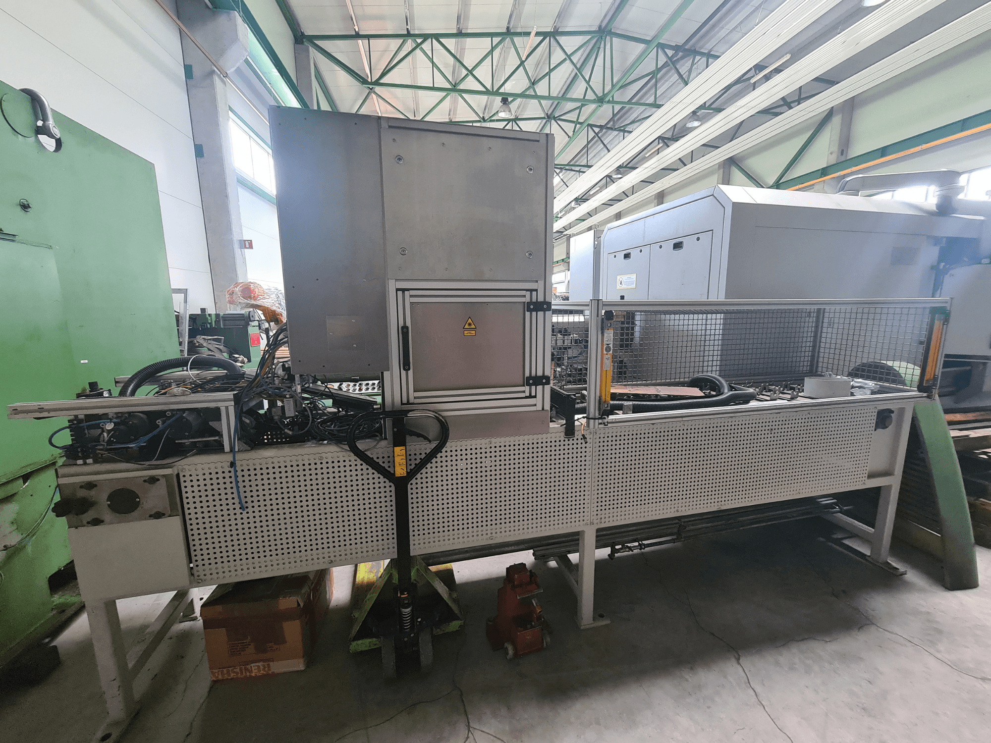 Industrial machinery with a metal frame, hoses, and control panel, viewed from the side in a factory setting.