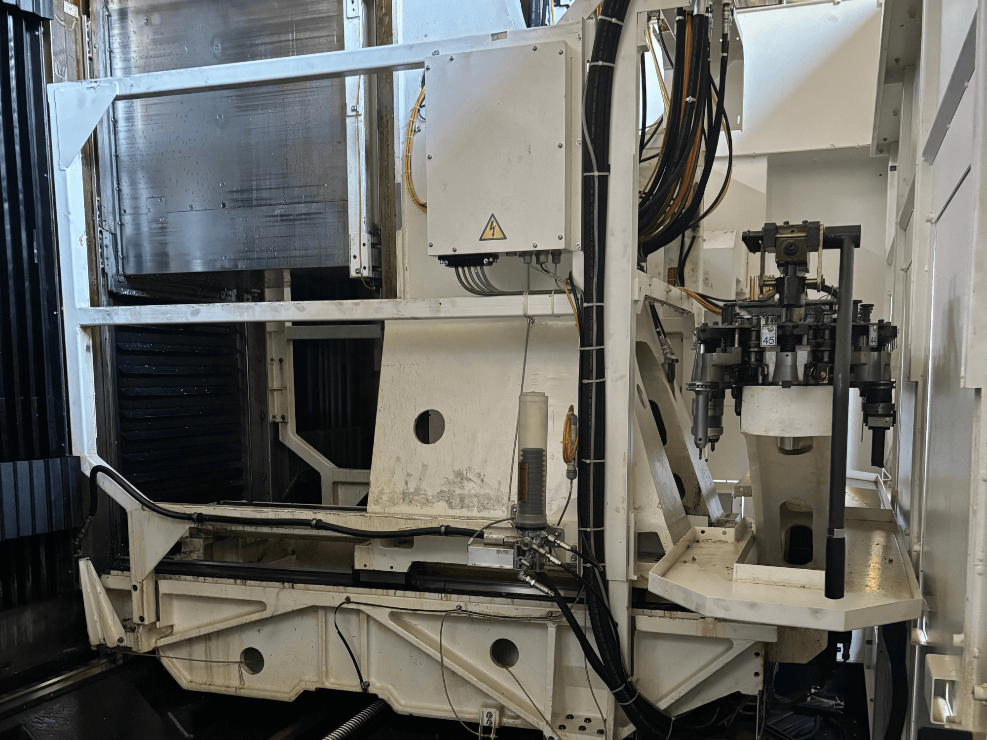 Industrial machine side view showing a white CNC milling machine with visible tools, pipes, and control panel.