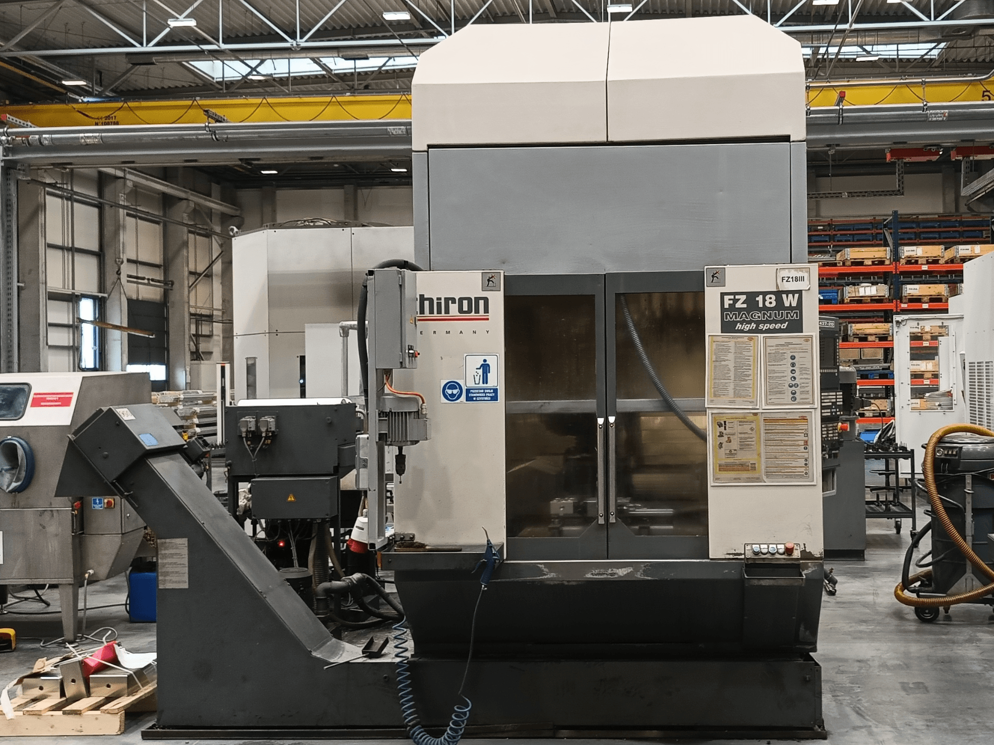Hiron FZ 18 W Magnum CNC-Maschine, Vorderansicht, mit Bedienelementen, Sicherheitsschildern und Industrieeinstellung mit Werkzeugen.