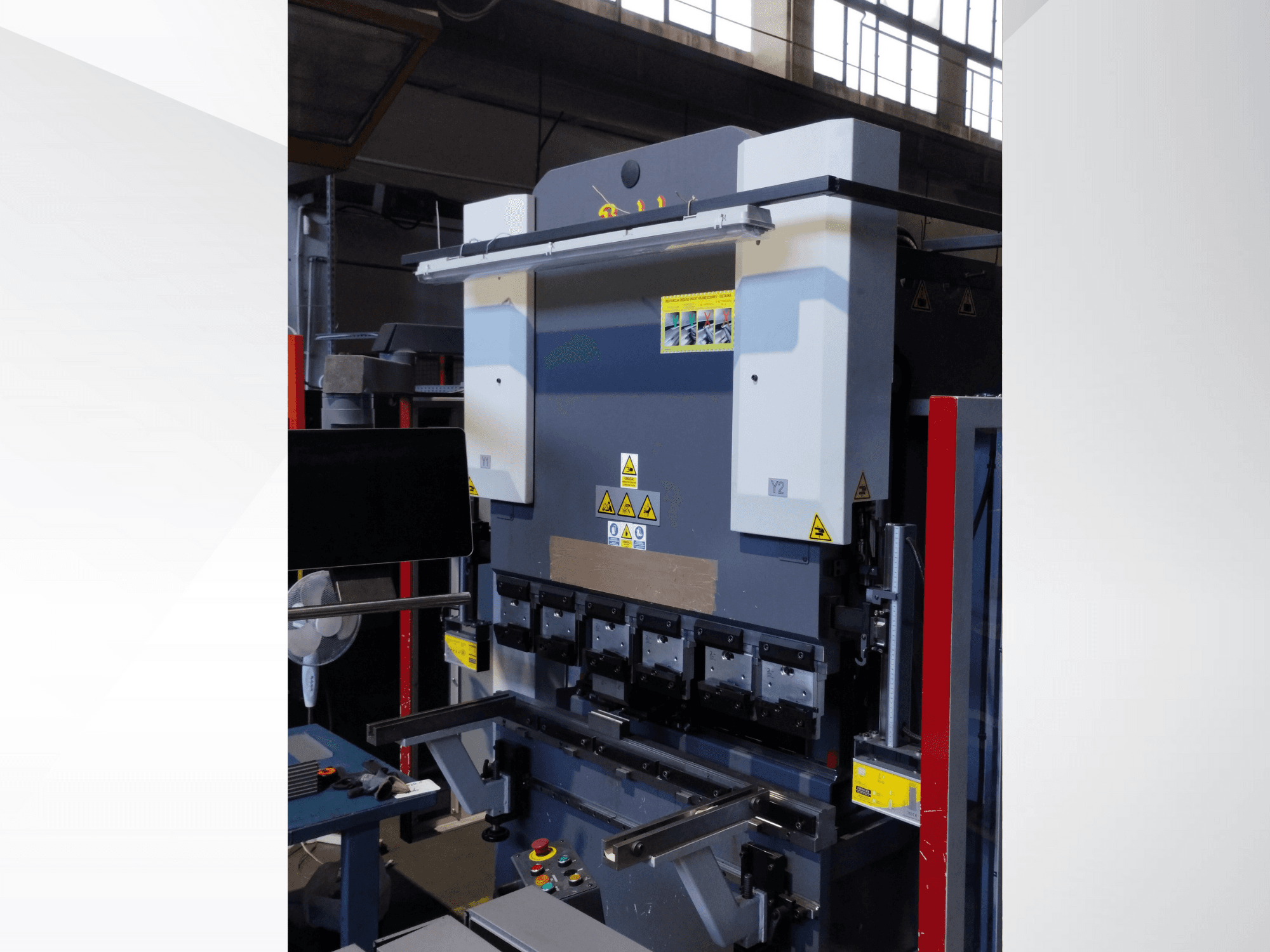 Abkantpresse, Vorderansicht. Mit sichtbaren Bedienelementen, Sicherheitsaufklebern und mehreren Matrizenhaltern für präzises Biegen.