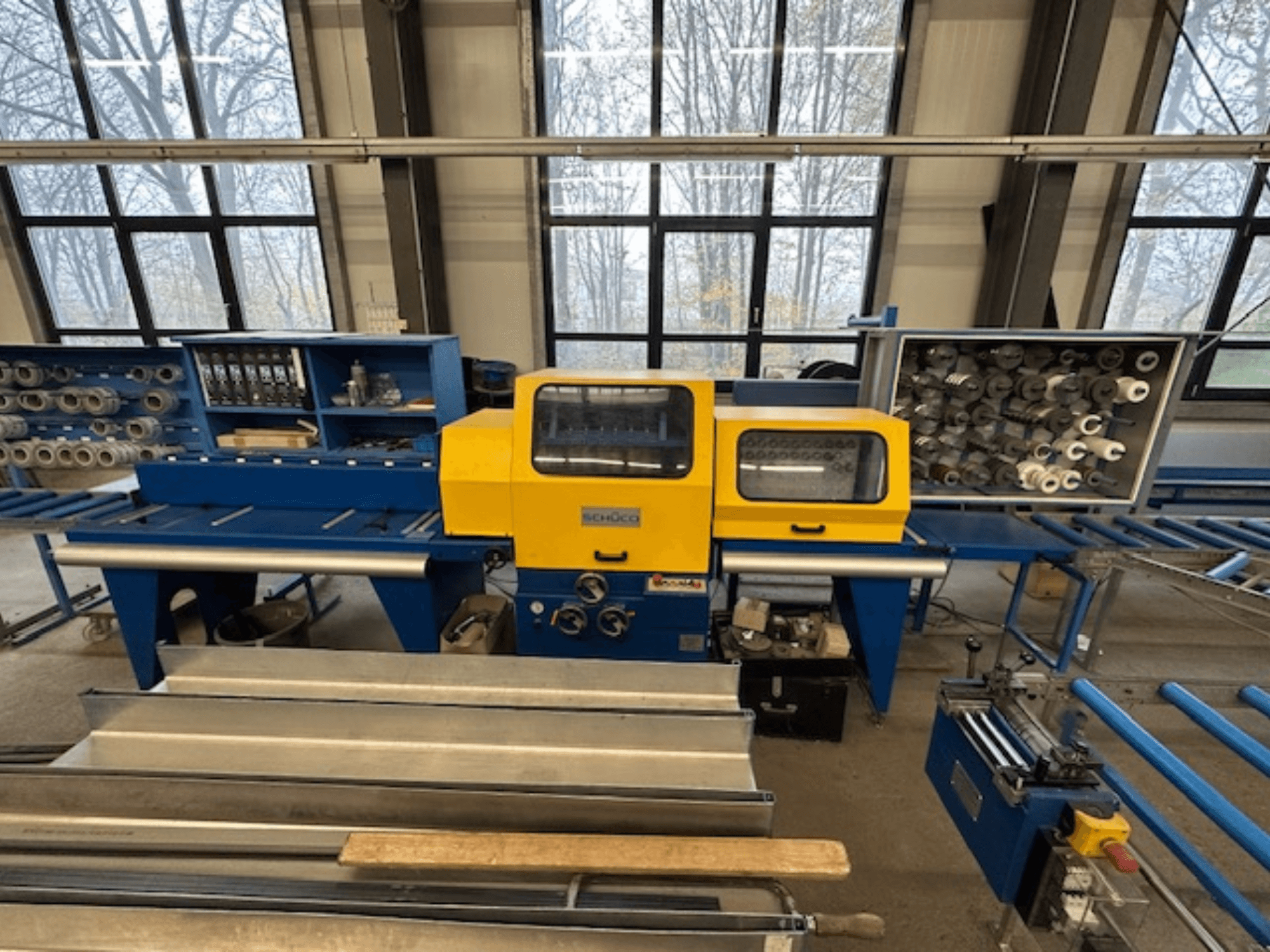 Vorderansicht der Werkzeugmaschine SCHÜCO ISOMAT 4 mit gelbem Bedienfeld, mehreren Walzen und einem Staufach.