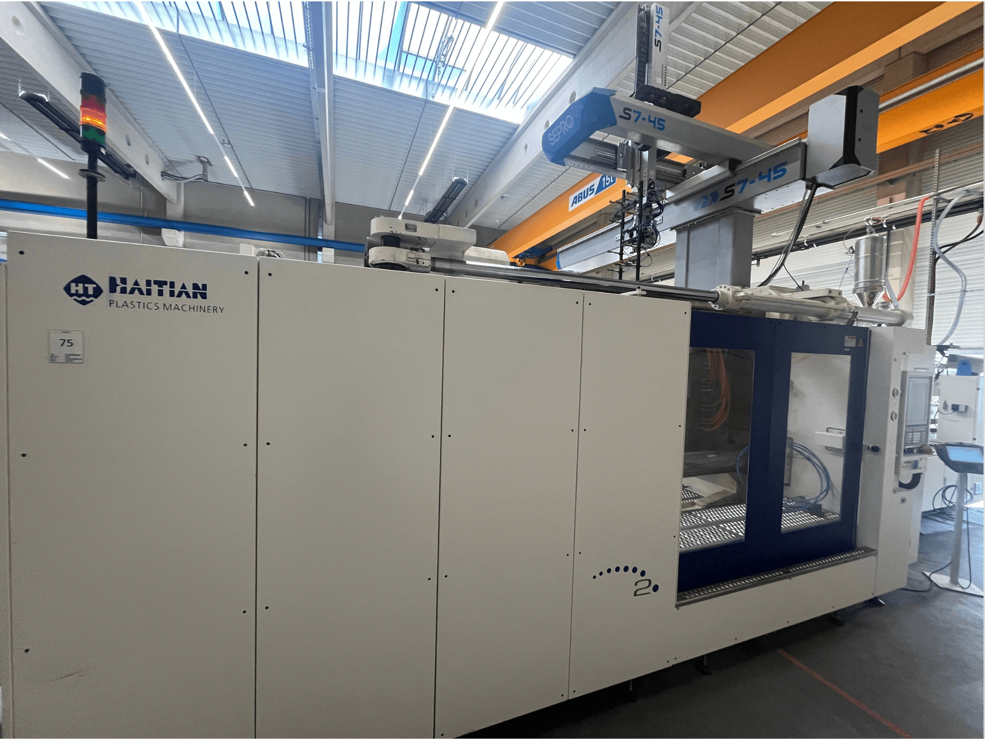 Haitianische Spritzgießmaschine S7-45 in der Seitenansicht mit Bedienfeld und Sicherheitslichtanzeige. Weißes und blaues Design.
