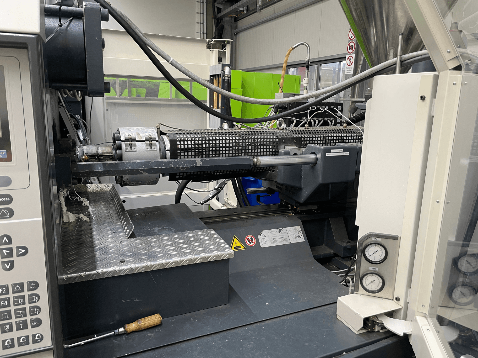 Injection molding machine side view with control panel, extruder, and pressure gauges visible, ideal for manufacturing tasks.