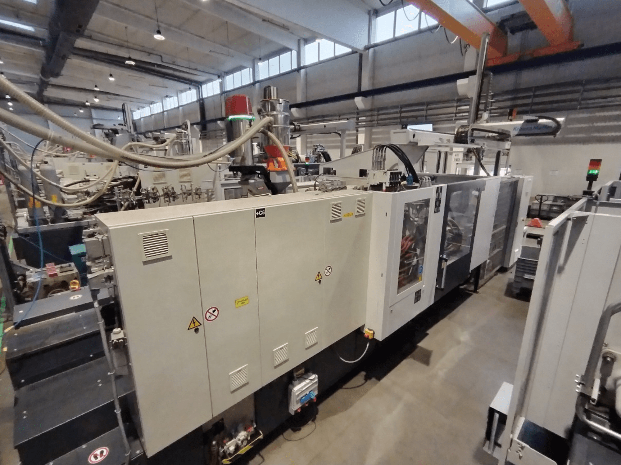 Industrial injection molding machine shown from a side view, featuring control panel and safety warnings. Brand: Unknown.