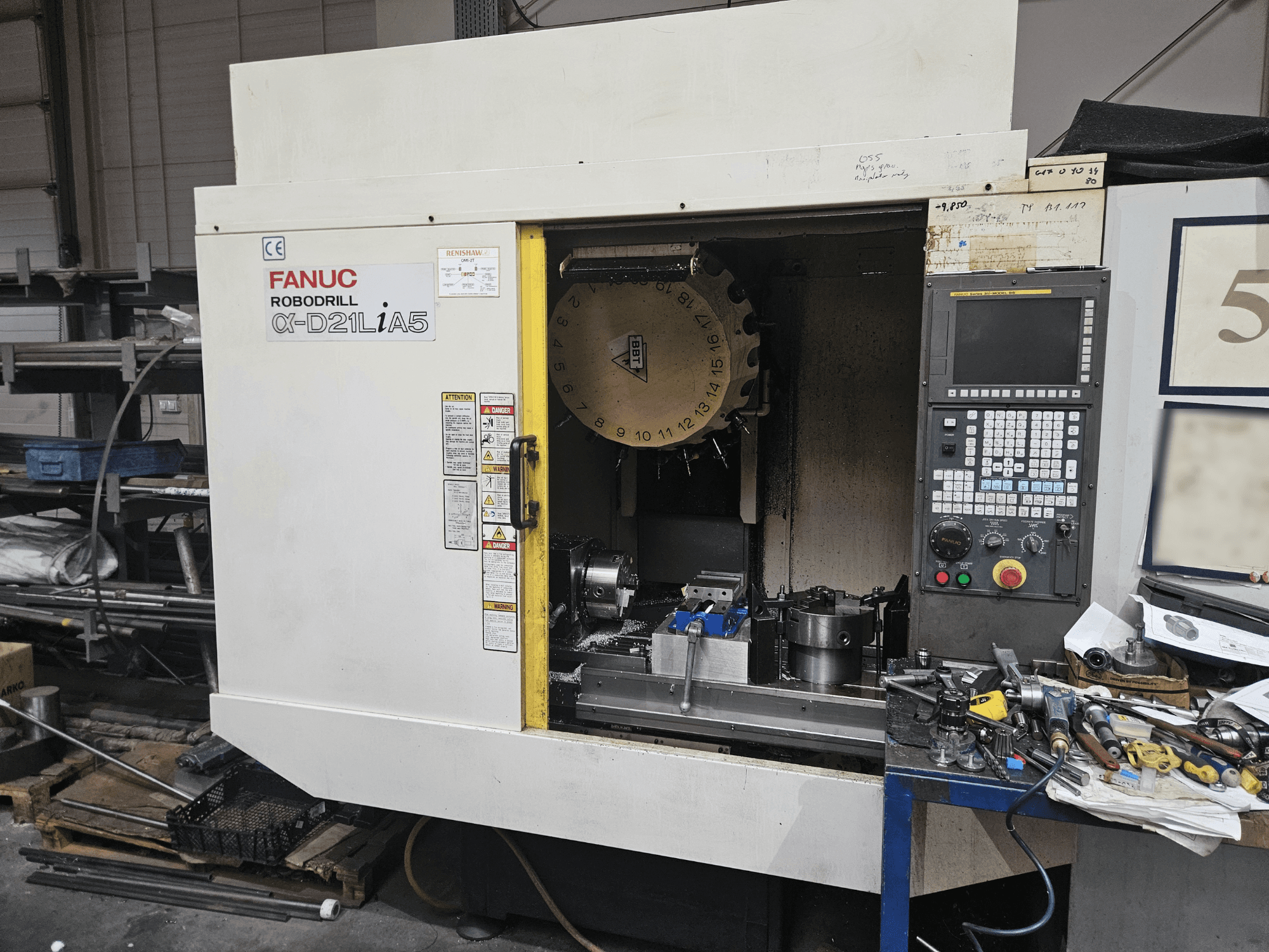 FANUC Robodrill α-D21LiA5, front view showing tool holder and control panel, surrounded by tools and equipment in a workshop.