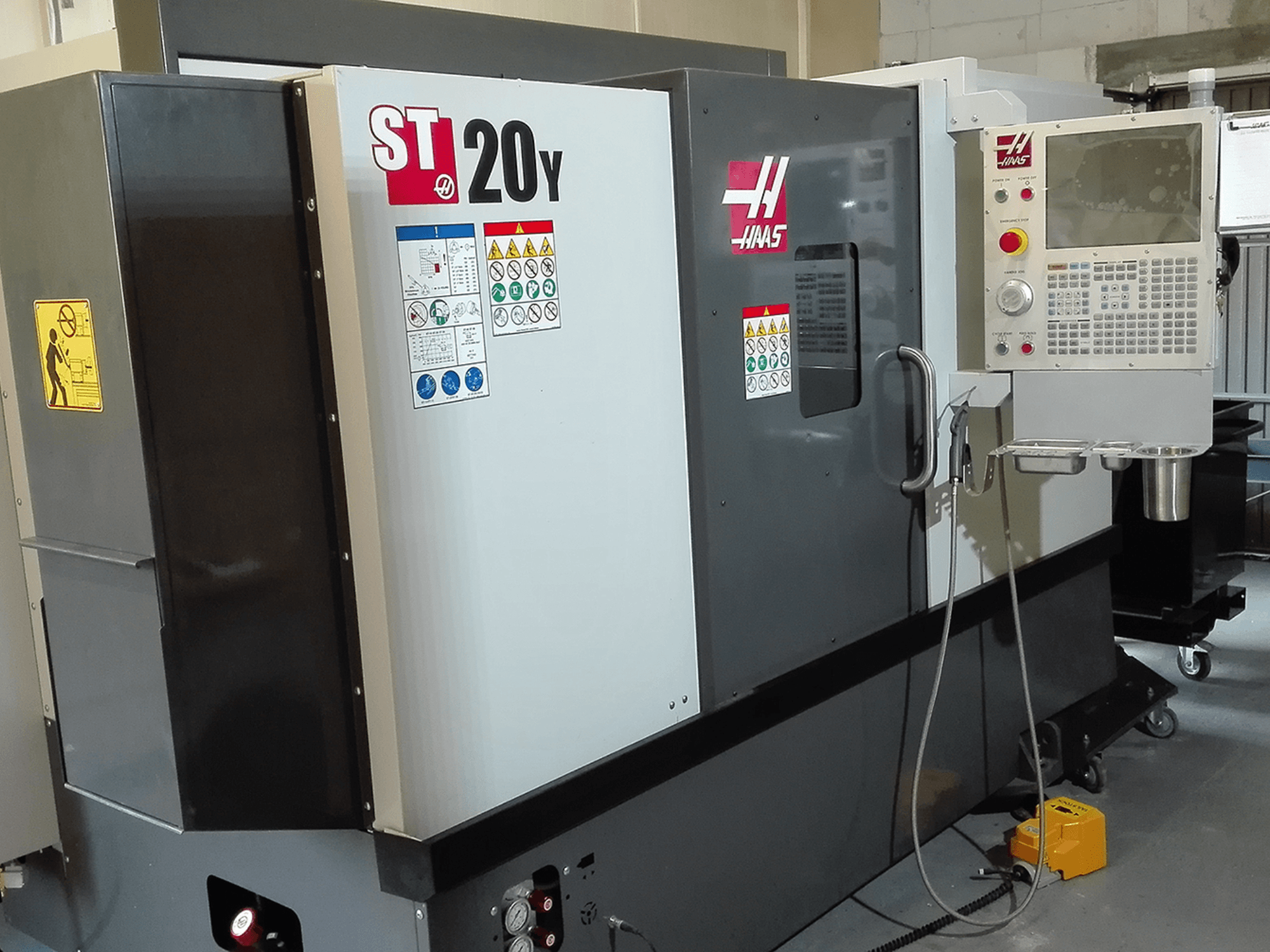 Haas ST20Y CNC-Drehmaschine in der Vorderansicht, mit Bedienfeld, Sicherheitsschildern und Kühlmittelanlage.
