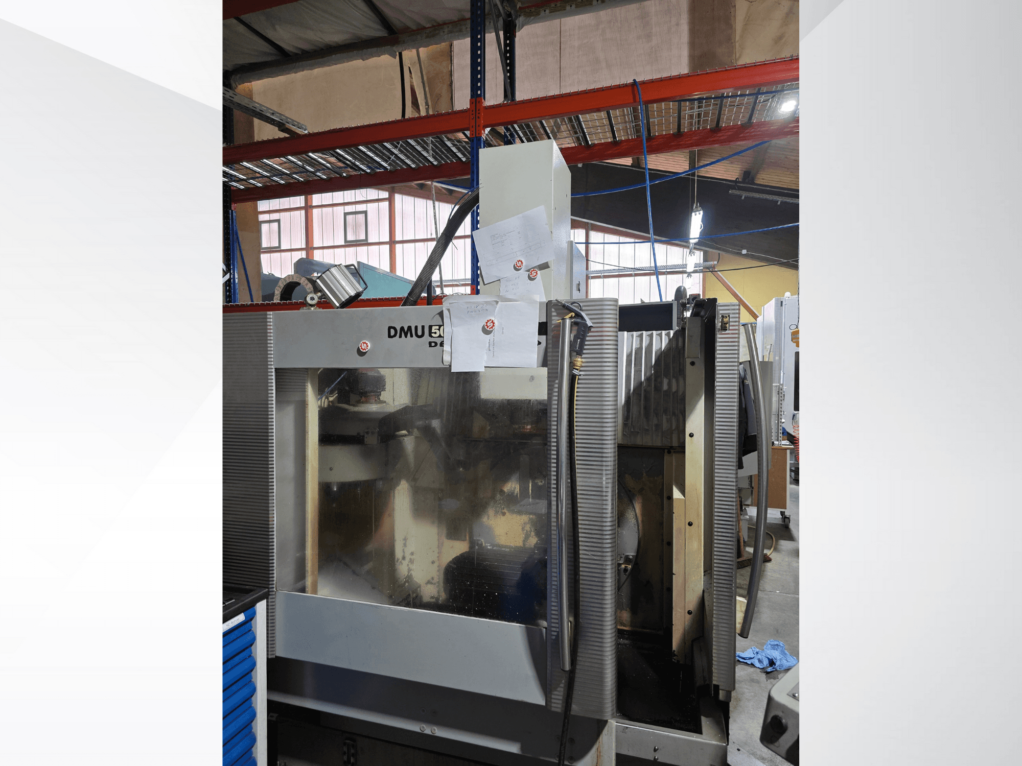 DMU 50 3-axis CNC machining center in a workshop, shown from the front, displaying operational components and documents attached.