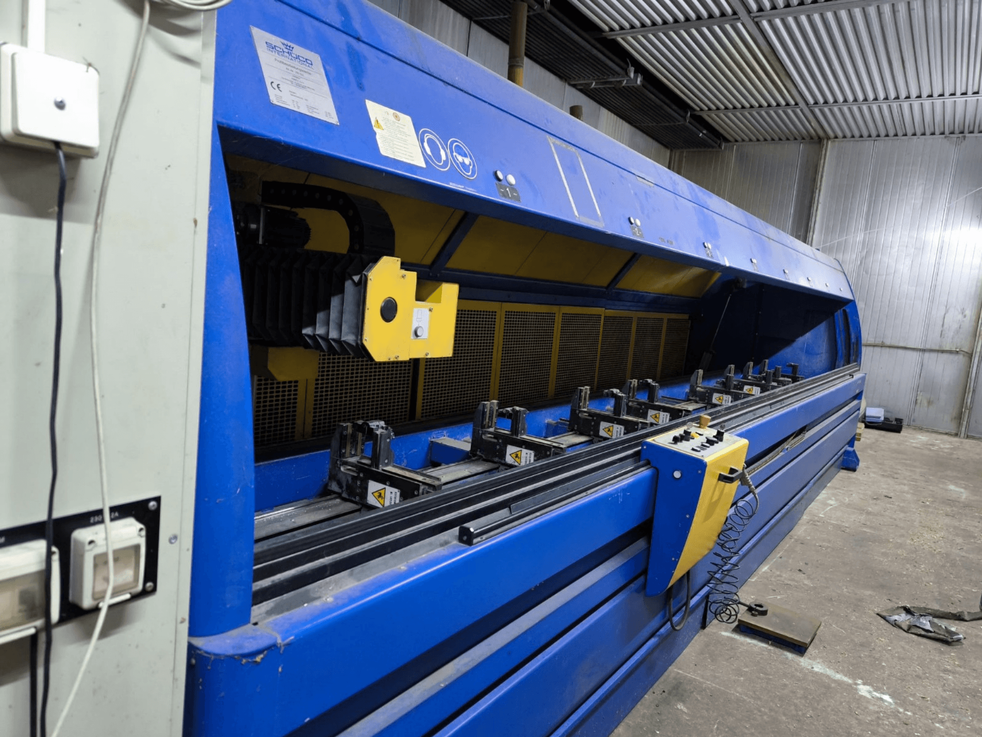 Schneider Industrie-Schneidemaschine in Blau, Seitenansicht, mit Bedienfeld, Bändern und mehreren Spannstationen.