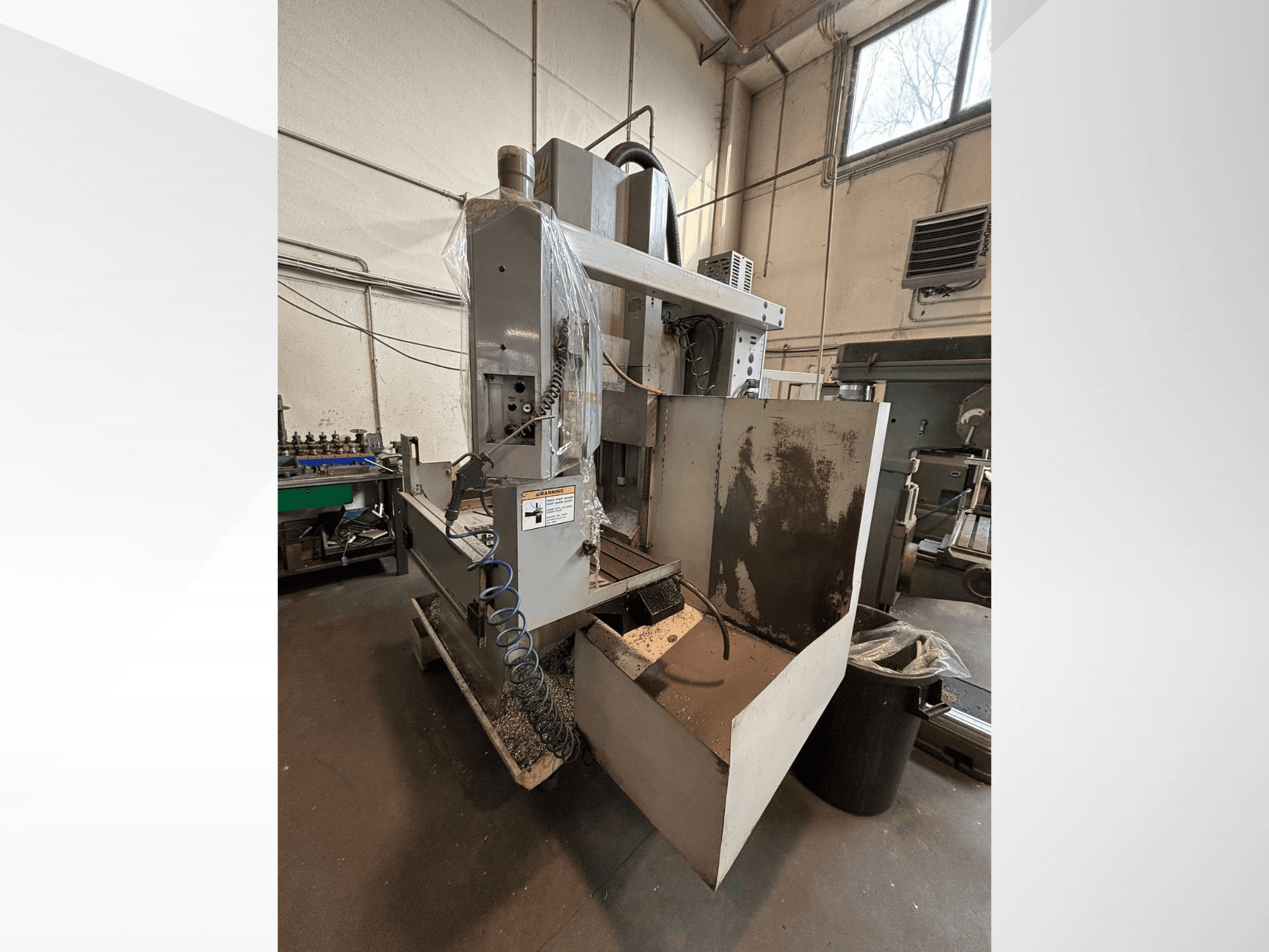 Vertical milling machine with protective cover, side view; includes coolant hose and control panel visible. Ideal for machining.