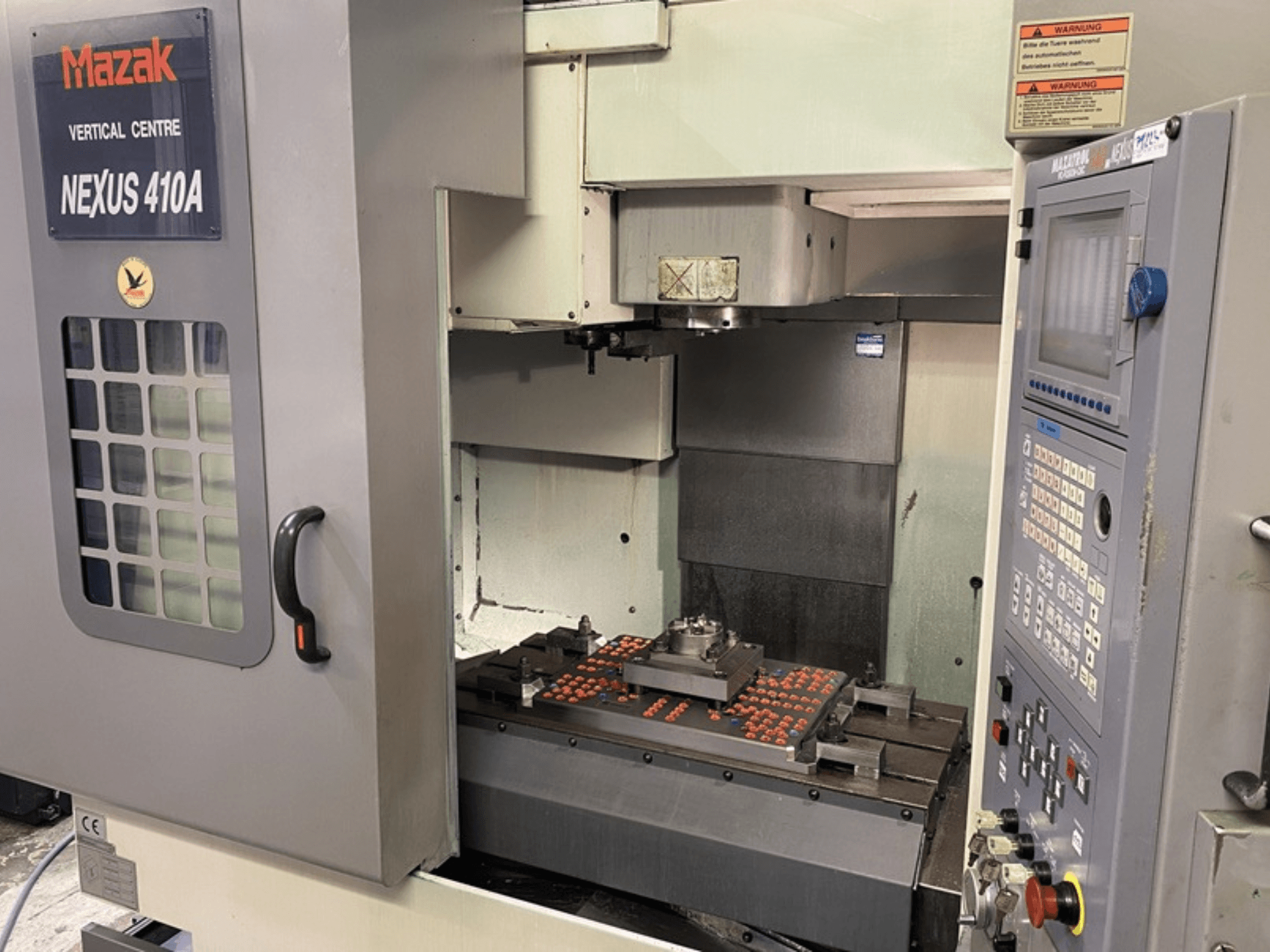 Mazak NEXUS 410A Vertikal-Bearbeitungszentrum, Vorderansicht, mit sichtbarem Bedienfeld und Werkzeugmaschineneinrichtung auf dem Arbeitsbereich.