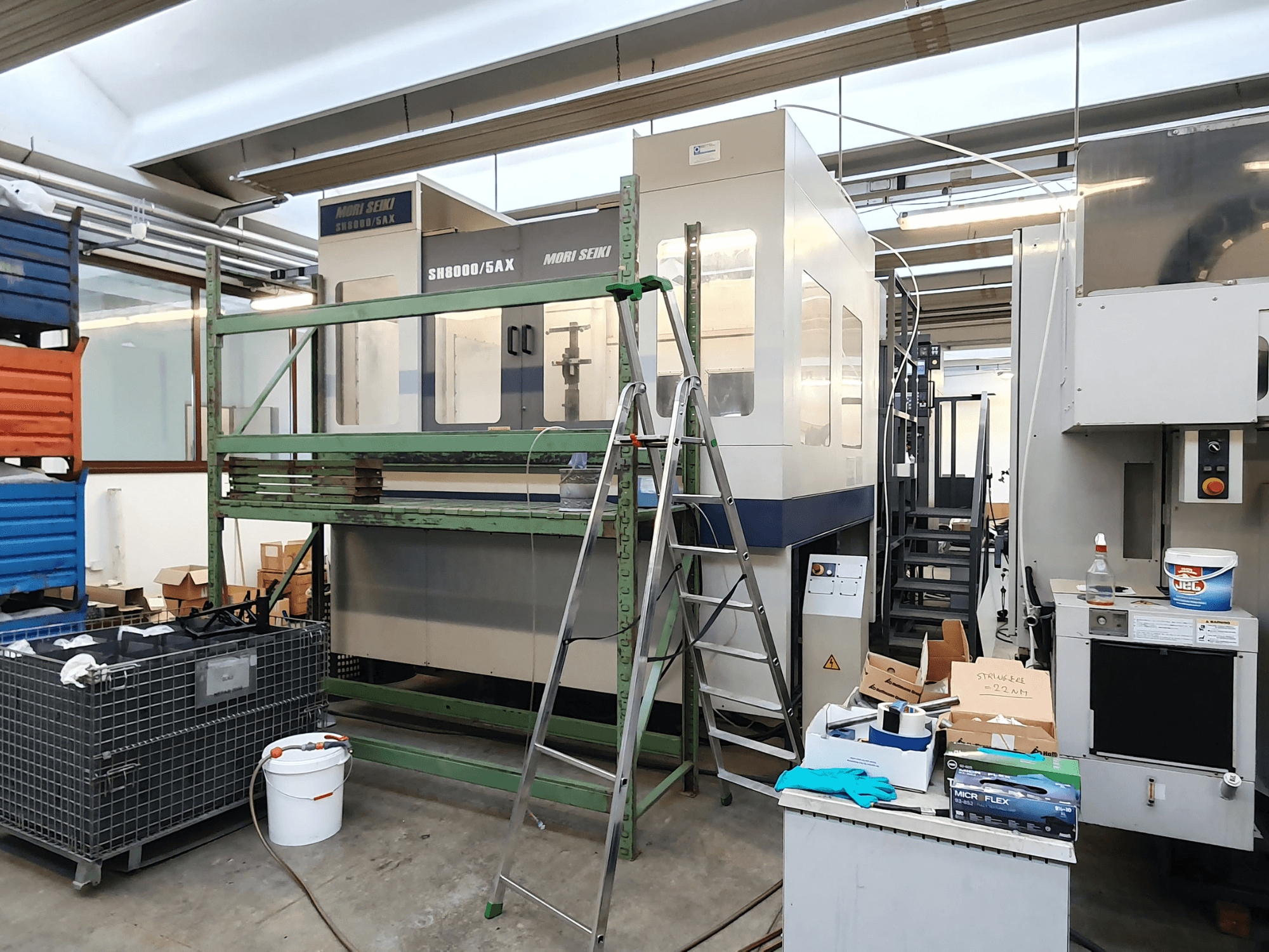 Mori Seiki SH-8000/5AX CNC-Maschine in einer Werkstatt, Vorderansicht, mit Werkzeugen und Lagerkästen in der Nähe.