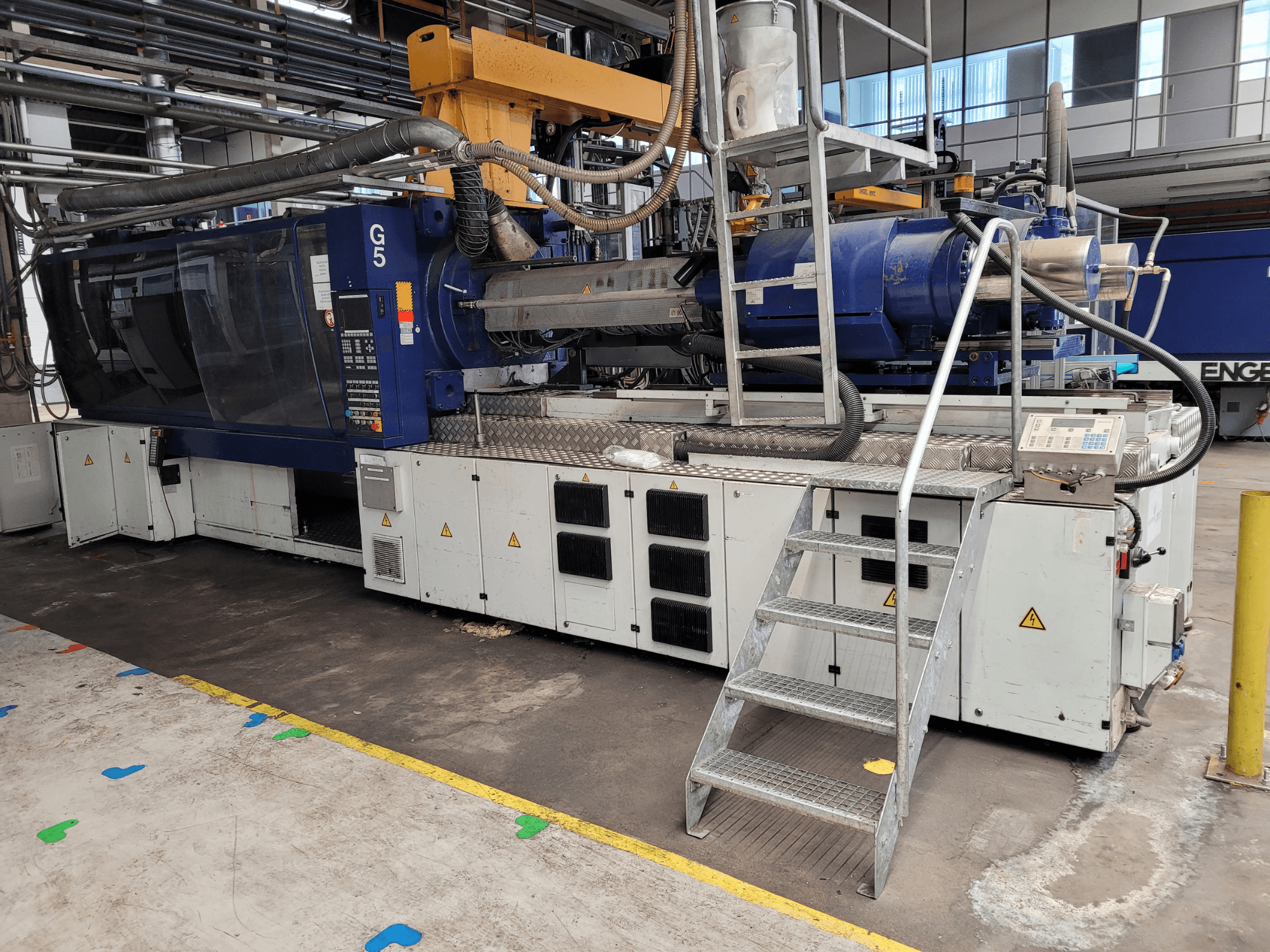 Spritzgießmaschine G5, Seitenansicht, mit Bedienpult, Trittleiter und Arbeitsfläche aus Edelstahl sichtbar.