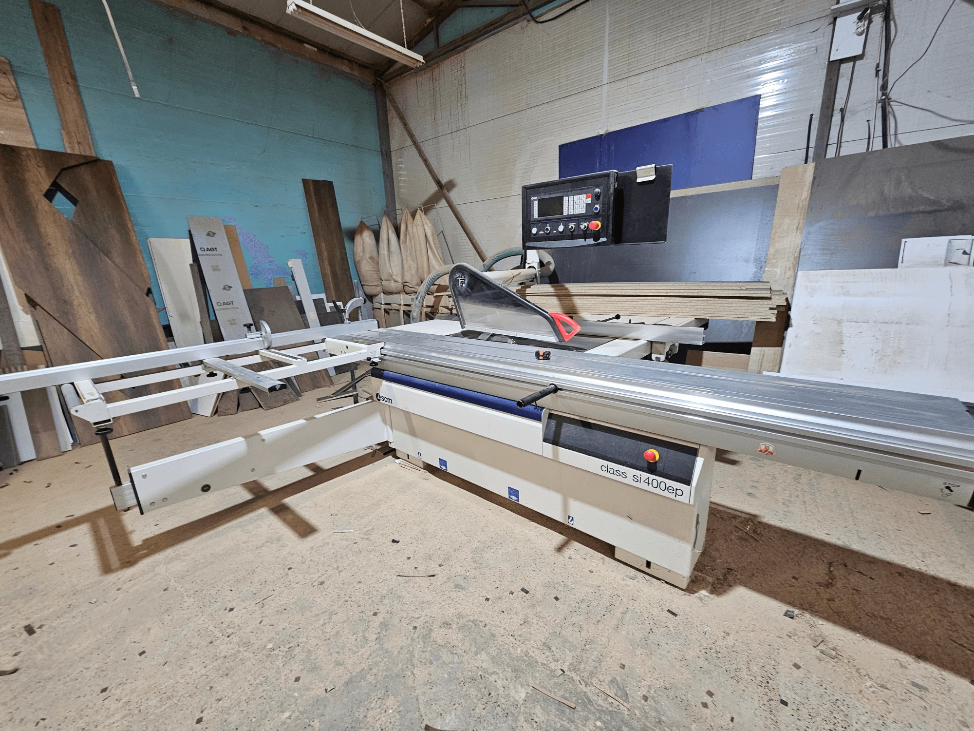 Plattensäge der Klasse SI400EP, Vorderansicht, mit verstellbarem Anschlag, aufgestellt auf sandigem Werkstattboden, umgeben von Holzplatten.