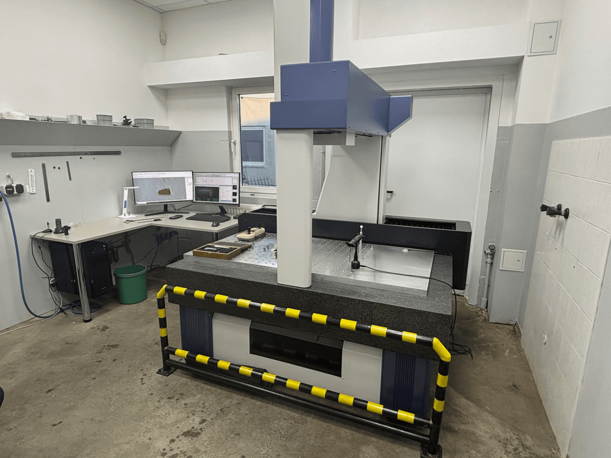 CMM workstation with measuring machine, dual monitors, and safety barriers. Front view showing equipment and setup details.