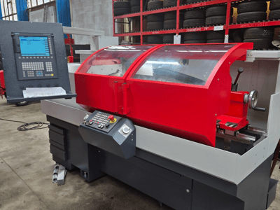 Rote CNC-Drehmaschine mit Bedienfeld, Vorderansicht; mit transparenter Abdeckung, Werkzeughalter und Ablagefächern.