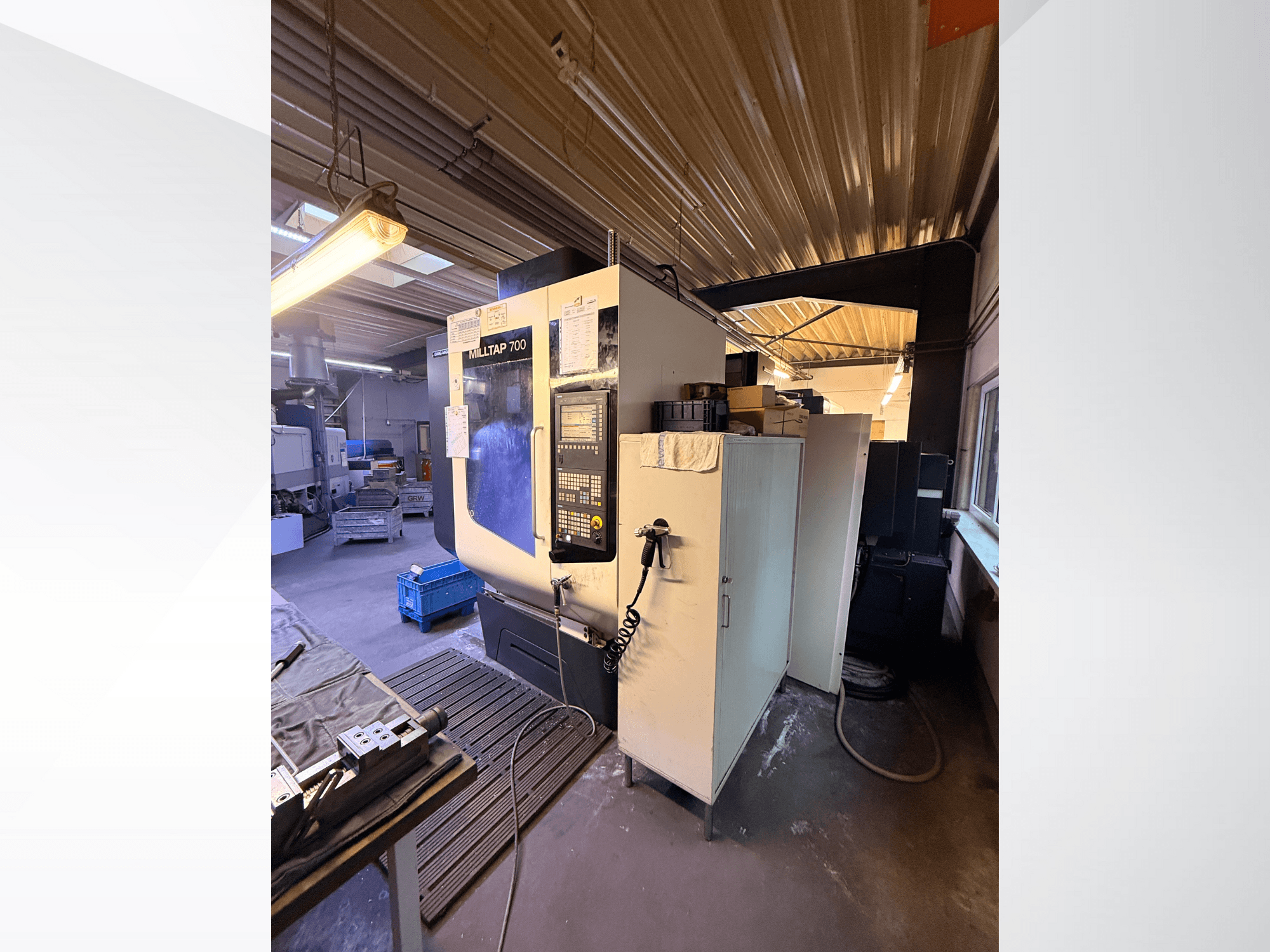Milltap 700 CNC-Maschine in der Werkstatt; Vorderansicht zeigt Bedienfeld, Werkzeugregale und Lagerbereiche mit Beleuchtung darüber.