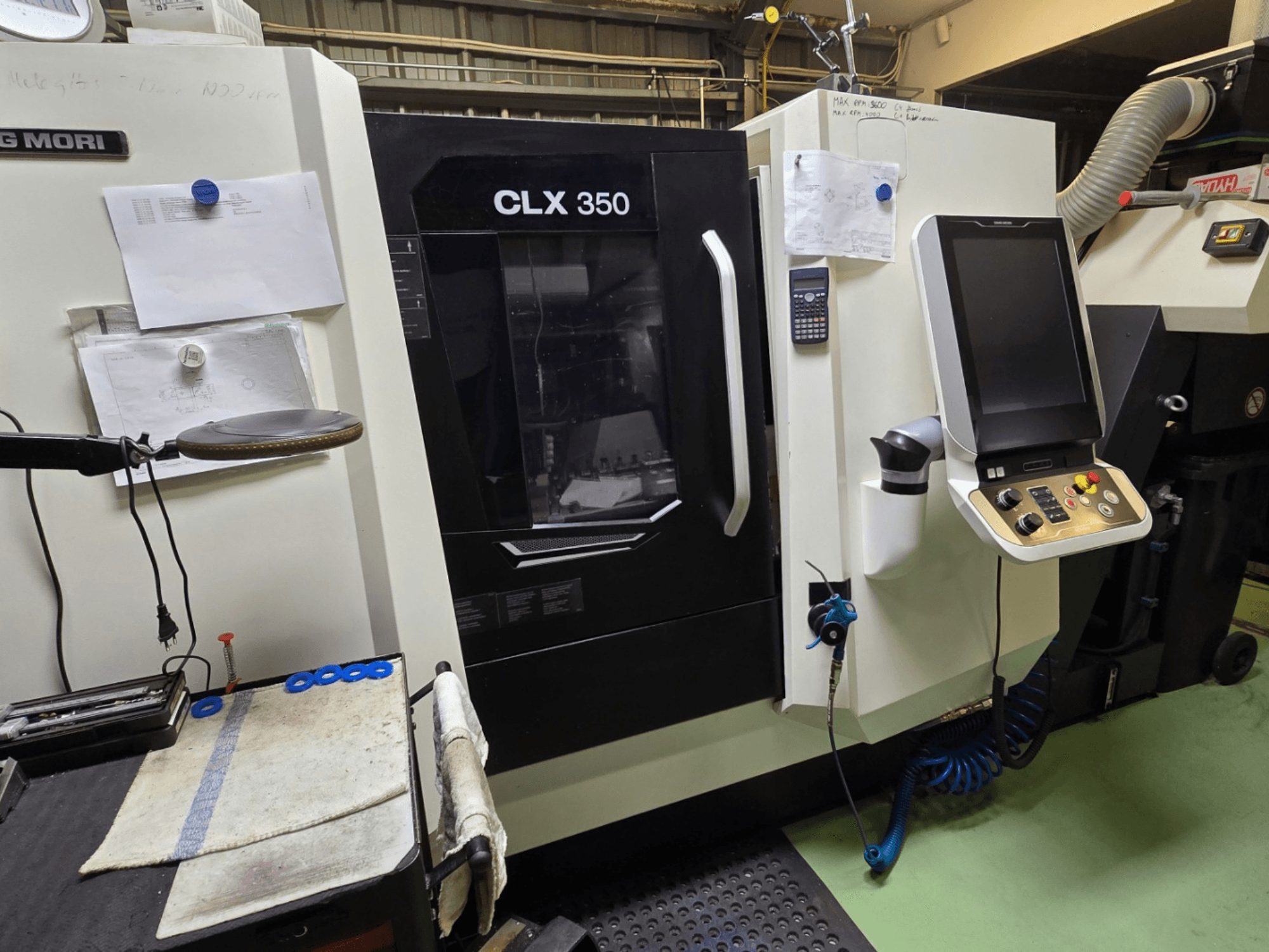 DMG MORI CLX 350 CNC-Drehmaschine in einer Werkstatt; Vorderansicht mit Bedienfeld, Werkzeugen und Arbeitsbereich.
