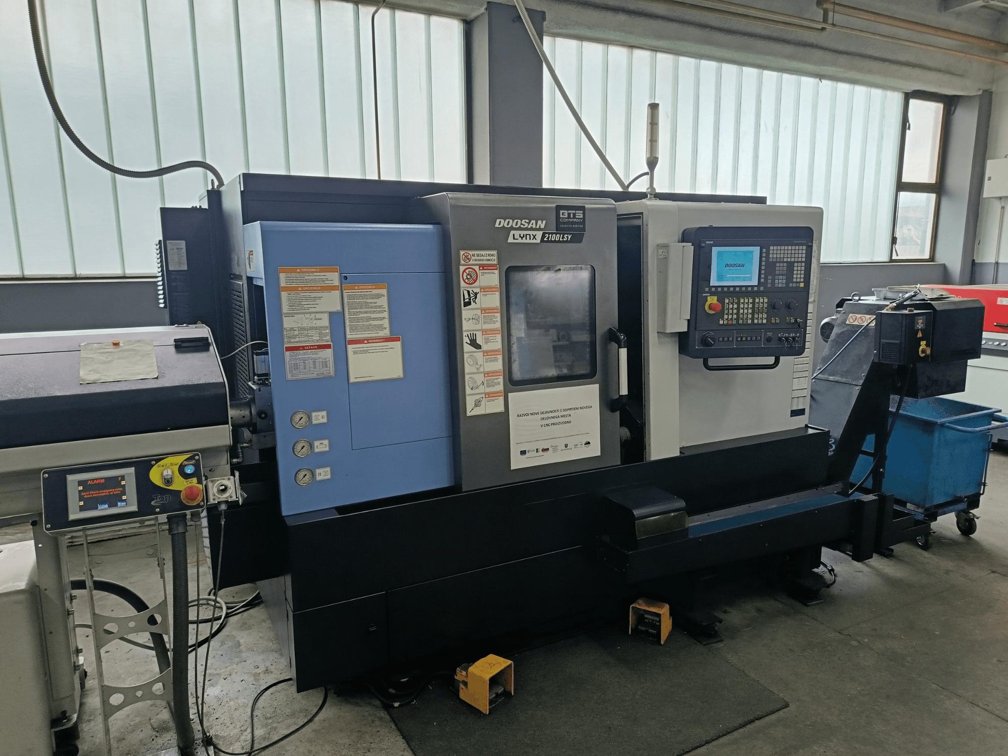 DOOSAN LYNX 2100 LSY Dreh-Fräszentrum, Seitenansicht mit Bedienfeld und Bedientasten, mit sichtbaren Informationsschildern.