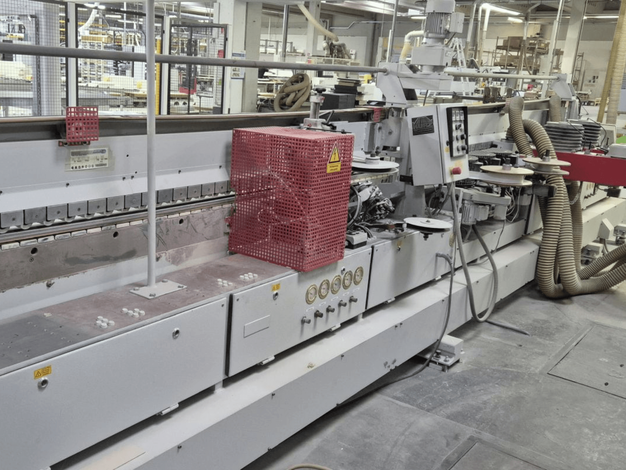 Kantenanleimmaschine mit Bedienfeld, Saugschläuchen und roter Sicherheitsabdeckung, von der Seite gesehen.