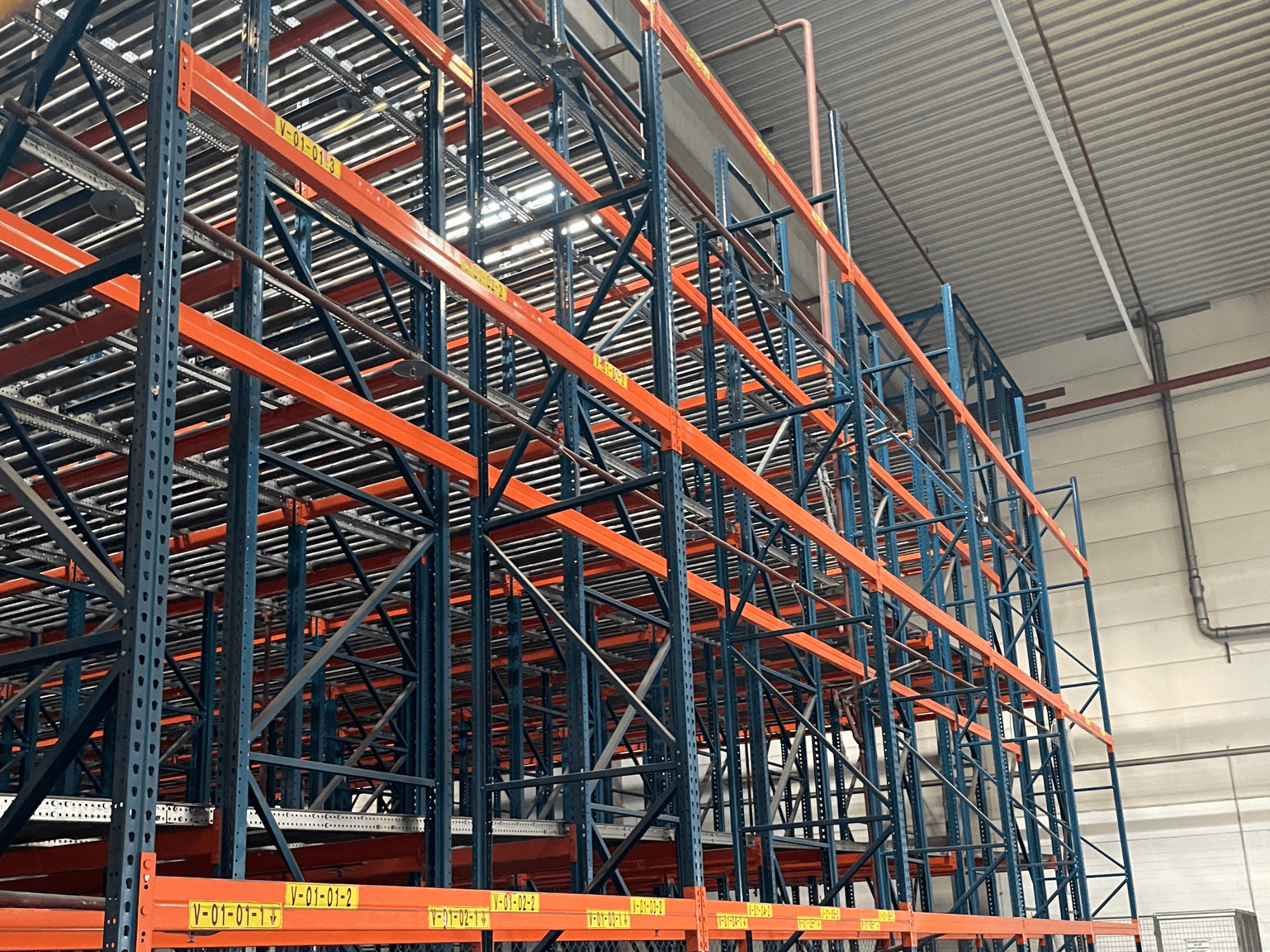 FL SYSTEME F05.10 FLG Palettenhandling-System in einem Lager, aus der Seitenansicht, mit orangen und blauen Schwerlastregalen.