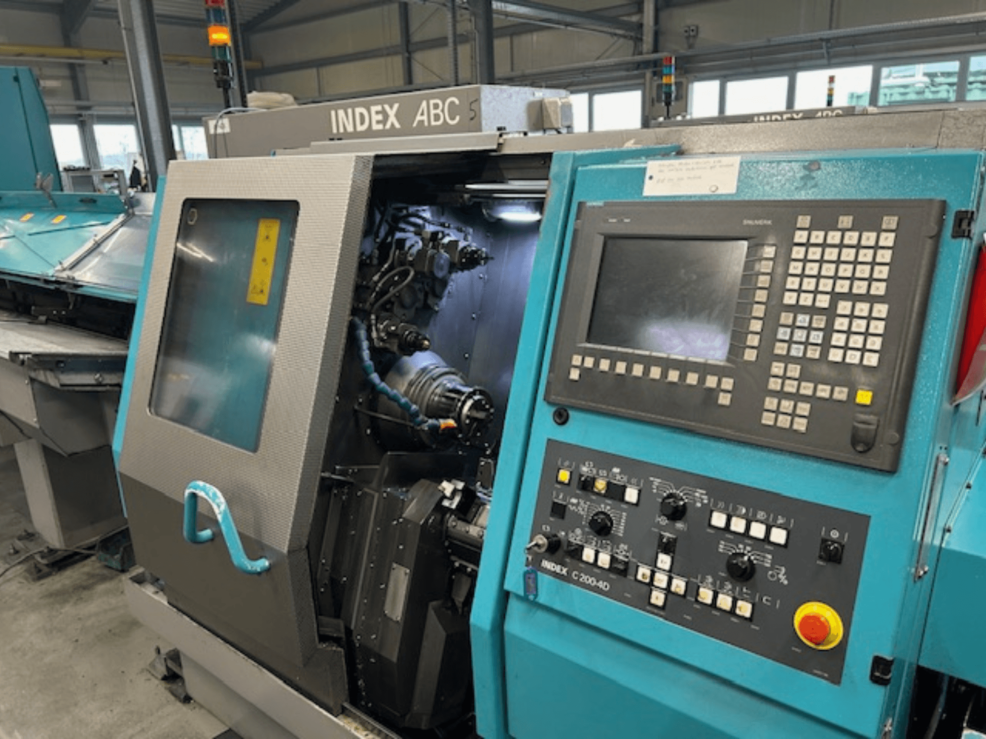 Frontansicht einer INDEX C200-AD CNC-Drehmaschine mit Bedienfeld, sichtbaren internen Komponenten und Sicherheitseinrichtungen.