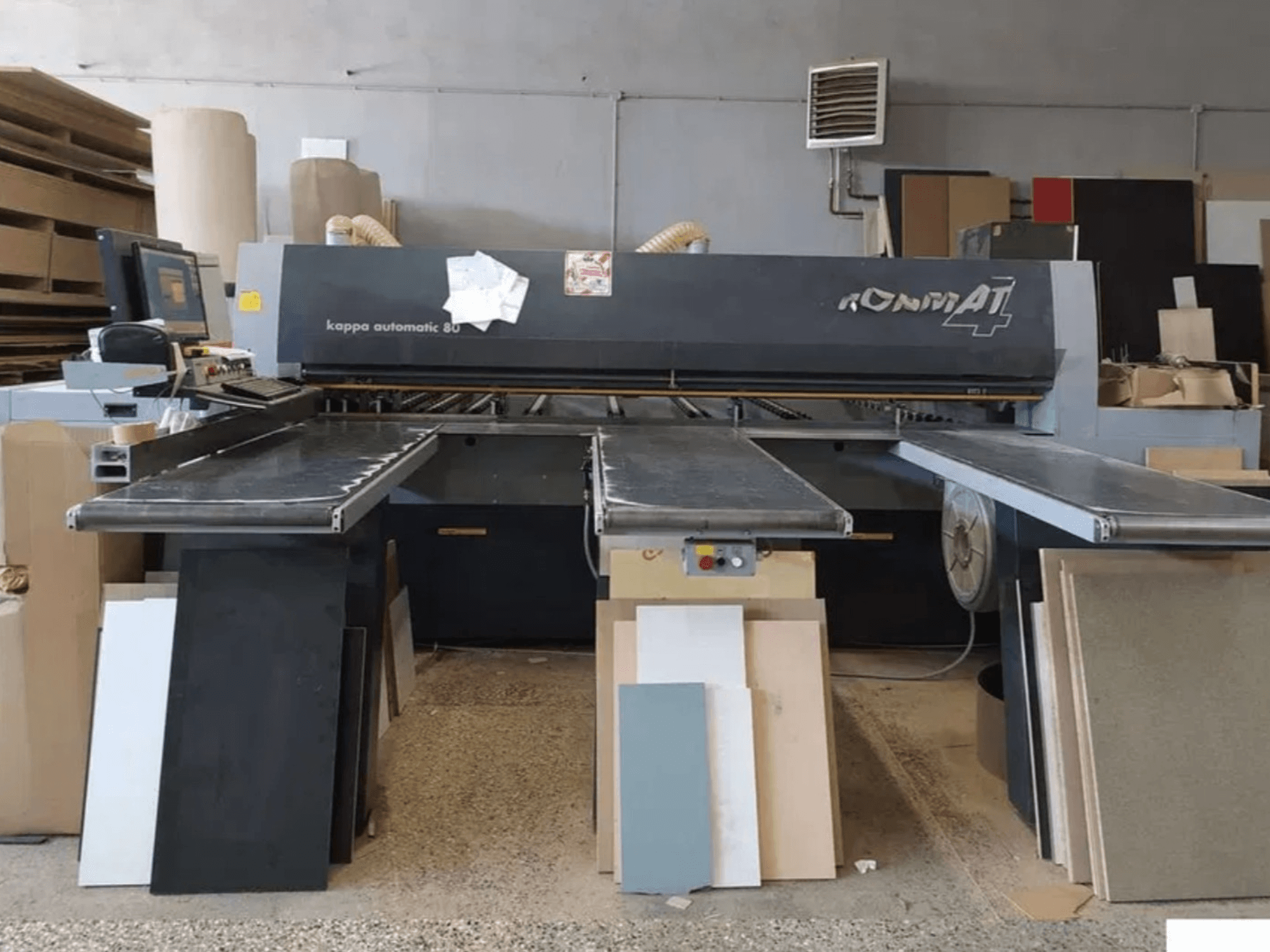 Kappa automatic 80 panel cutting machine, front view, with dual conveyor belts and assorted cut panels stacked beside it.