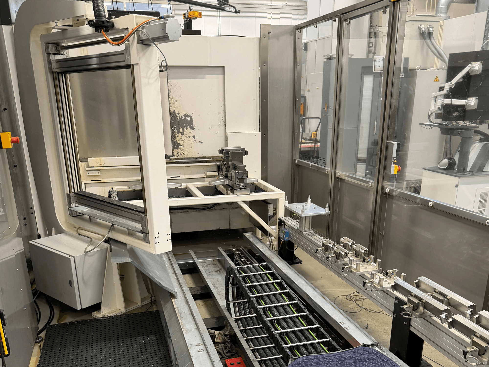 Automatisierter Industriearbeitsplatz mit einem Roboterarm, einem Schienensystem und einem Bedienfeld in der Seitenansicht.