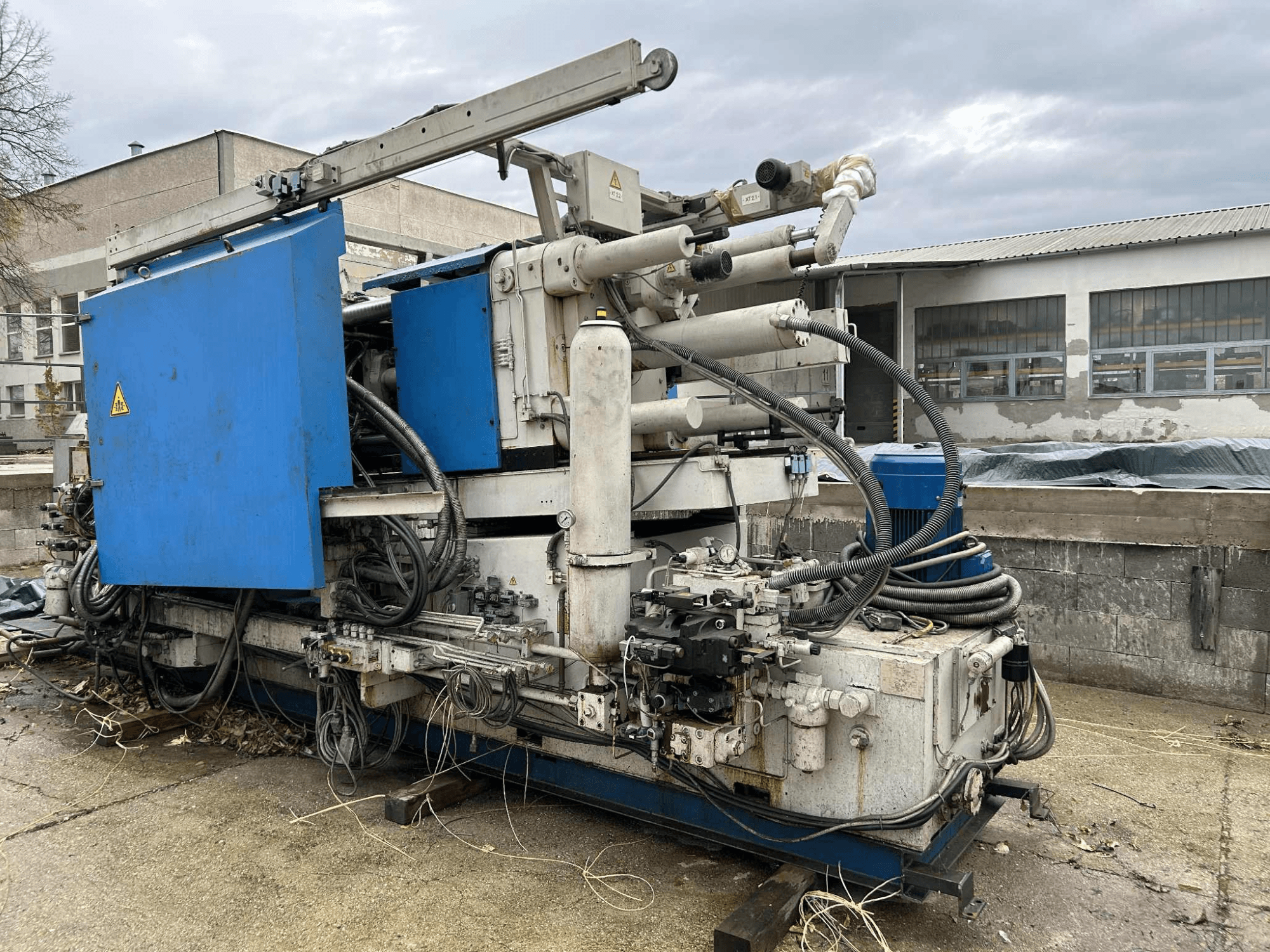 Große hydraulische Industriemaschine mit blauem Gehäuse, verschiedenen Schläuchen und Metallteilen, von der Seite gesehen.