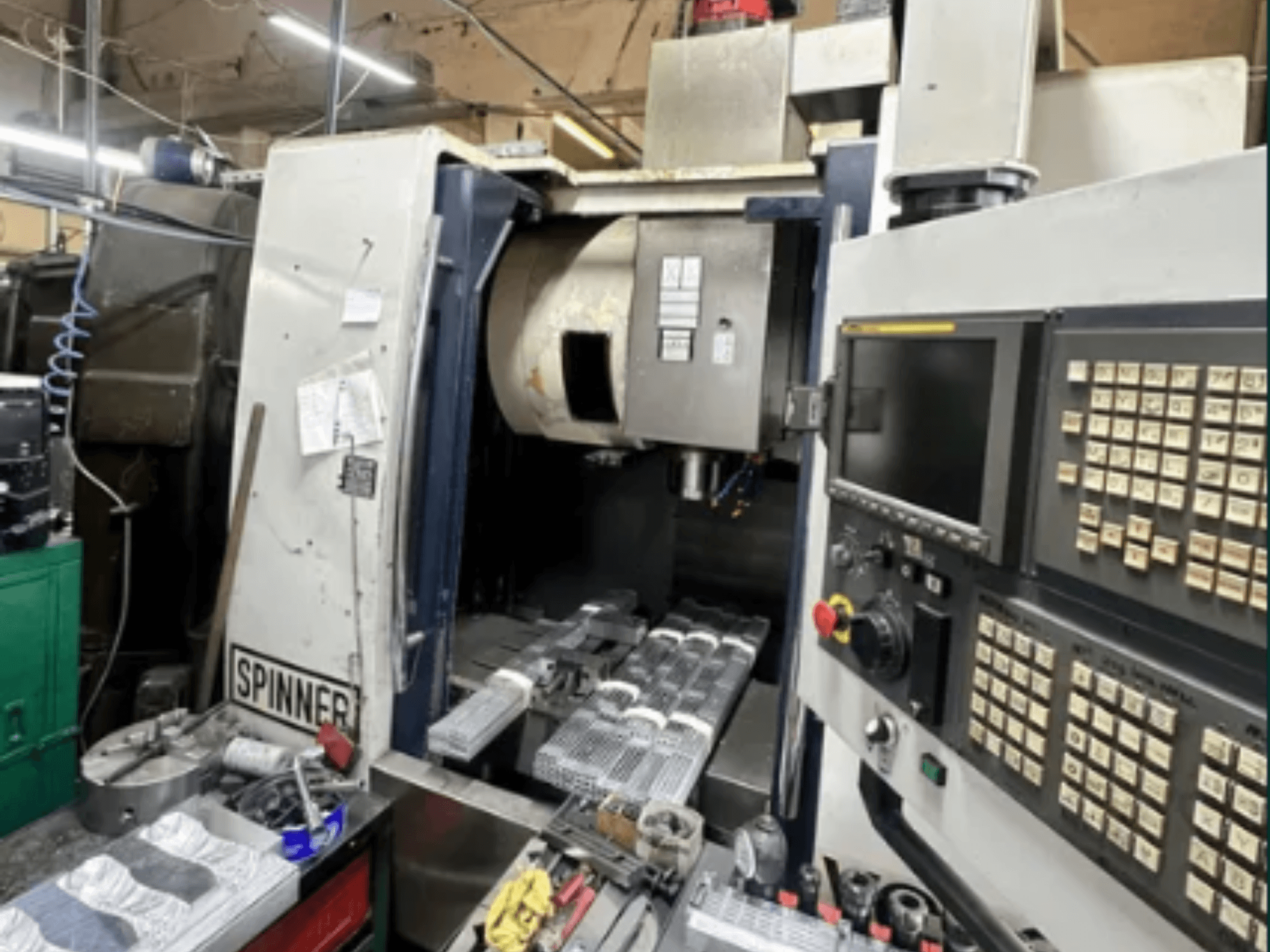 CNC-Maschine von Spinner, Vorderansicht; mit Touchscreen-Oberfläche, Werkzeugen auf der Arbeitsfläche und bearbeiteten Teilen, die zur Bearbeitung bereit sind.