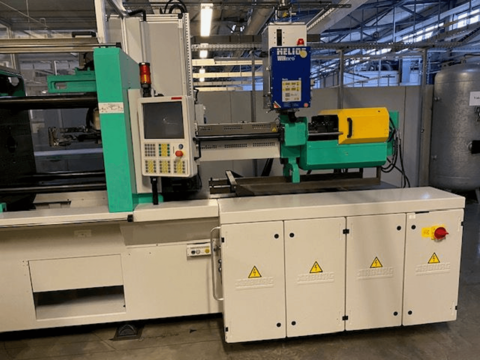 Industrielle Spritzgießmaschine, Modell HELIO, Vorderansicht, mit Bedienfeld, Schutzvorrichtungen und Not-Aus-Taste.